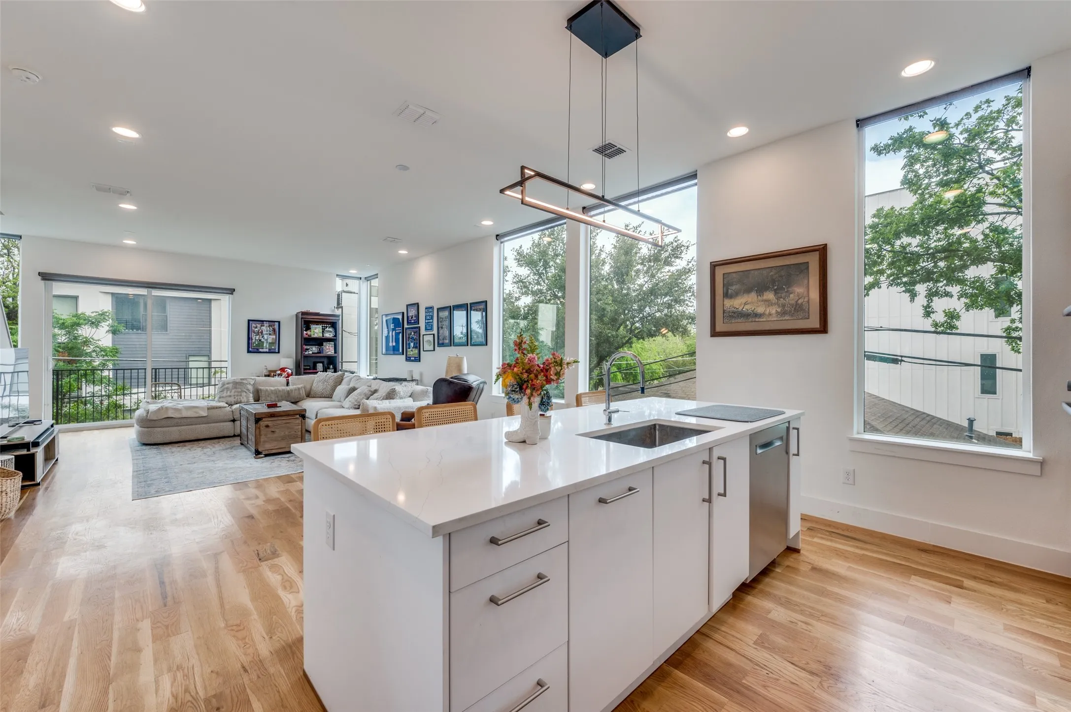 Open concept living space featuring hardwood floors, a kitchen island with a sink and a stainless steel dishwasher, and large windows providing natural light