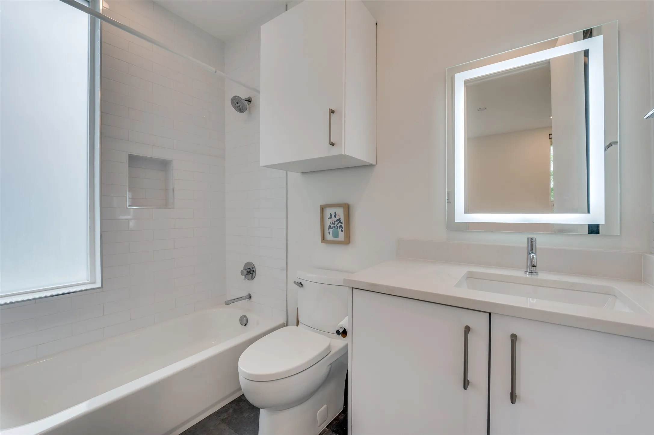 Bathroom featuring a white bathtub with subway tile surround, a built-in shower niche, and a vanity with an integrated sink and an illuminated mirror
