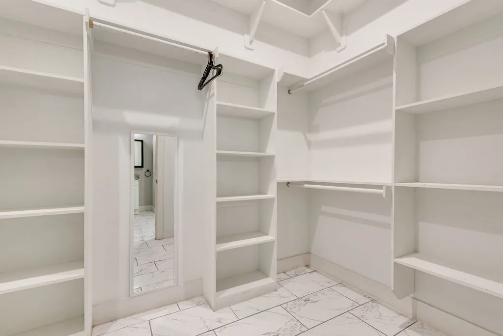 This walk-in closet features white shelving and hanging rods, along with a full-length mirror