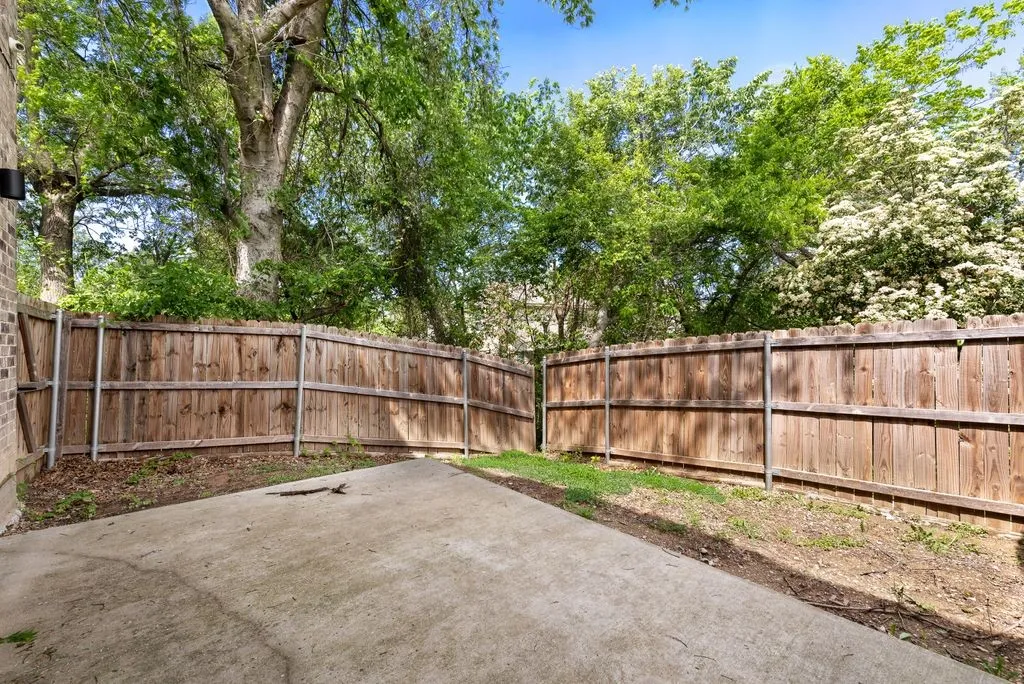 The property features a private yard with a wooden fence, a concrete patio, and mature trees providing natural shade