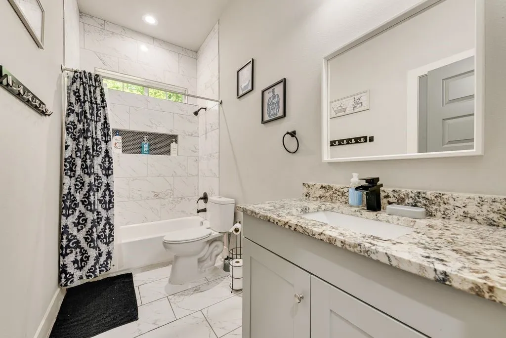 Bathroom featuring a white bathtub, tiled shower surround with a recessed niche, a window, and a vanity with a granite countertop and an undermount sink