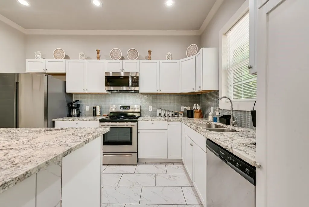 The kitchen features white cabinetry, stainless steel appliances, speckled countertops, and a tiled backsplash
