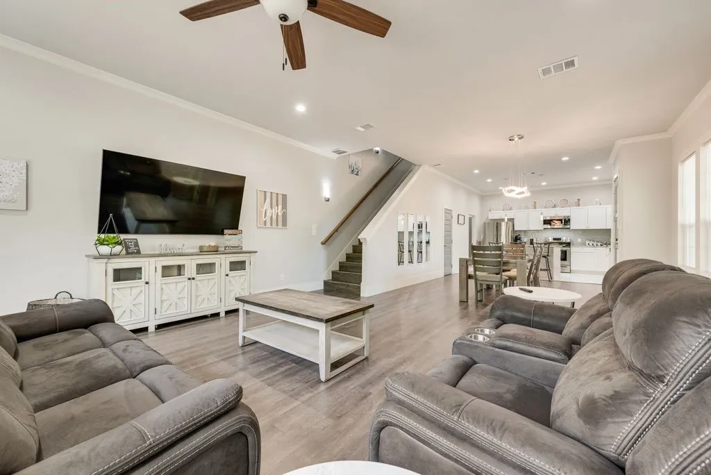 This living area features light-toned flooring, a ceiling fan, and crown molding