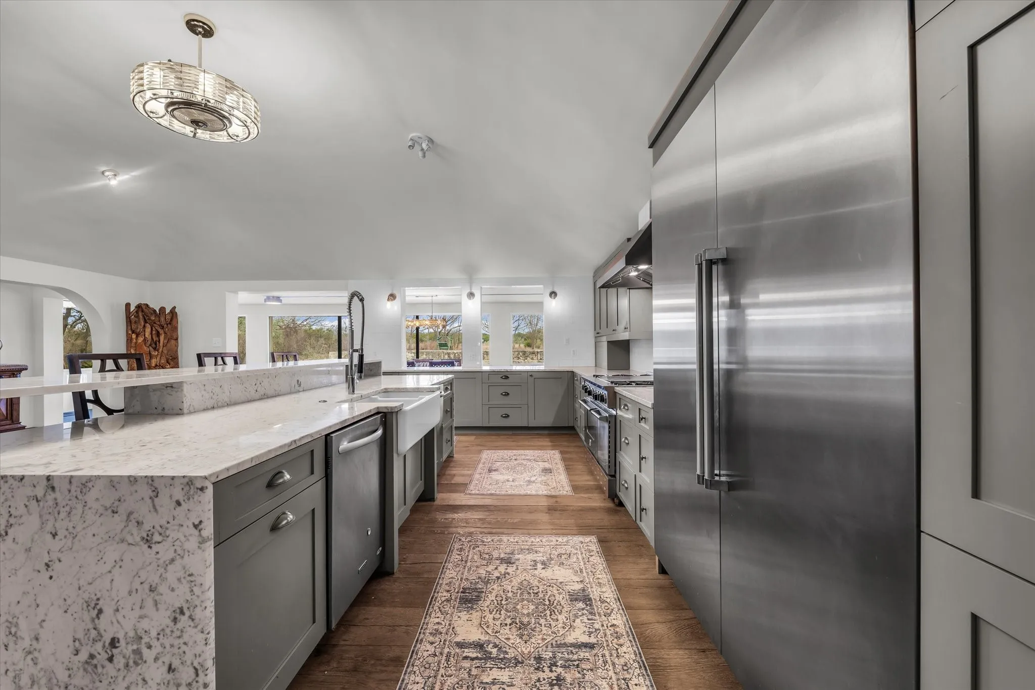 Kitchen with gray cabinetry, high quality appliances, light stone countertops, wood finished floors, and range hood