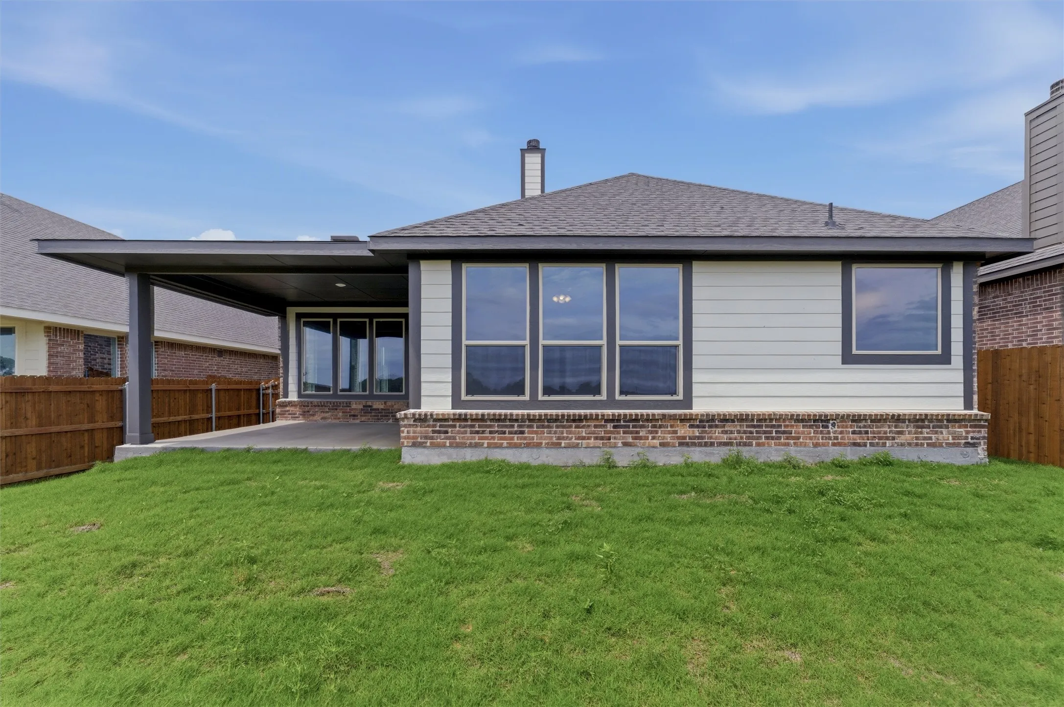 Expansive green lawn backing to a home featuring a covered patio, multiple windows, and a brick foundation