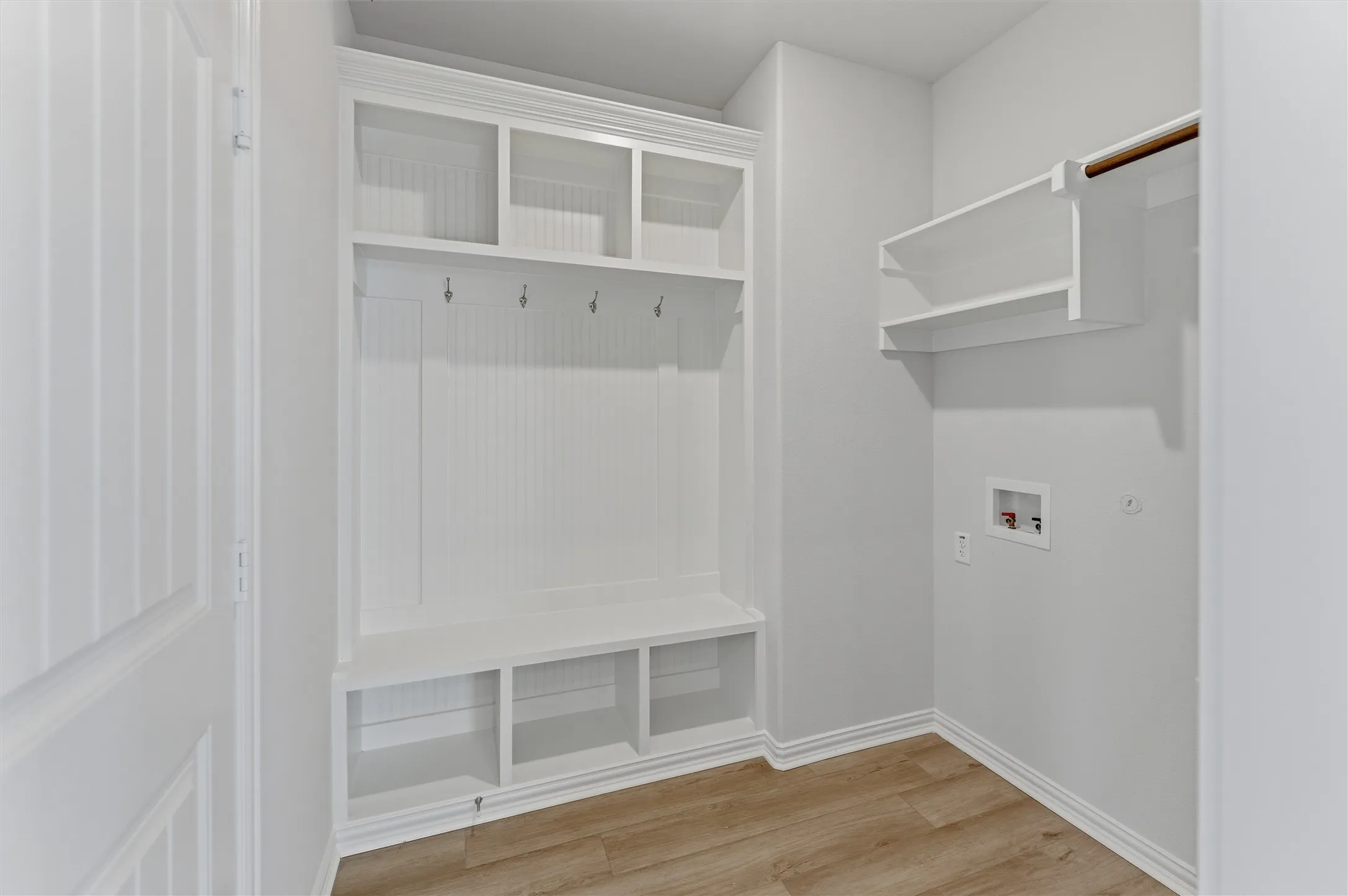 Dedicated utility area featuring wood-finish flooring, white built-in storage with cubbies, upper shelving, and a bench with coat hooks