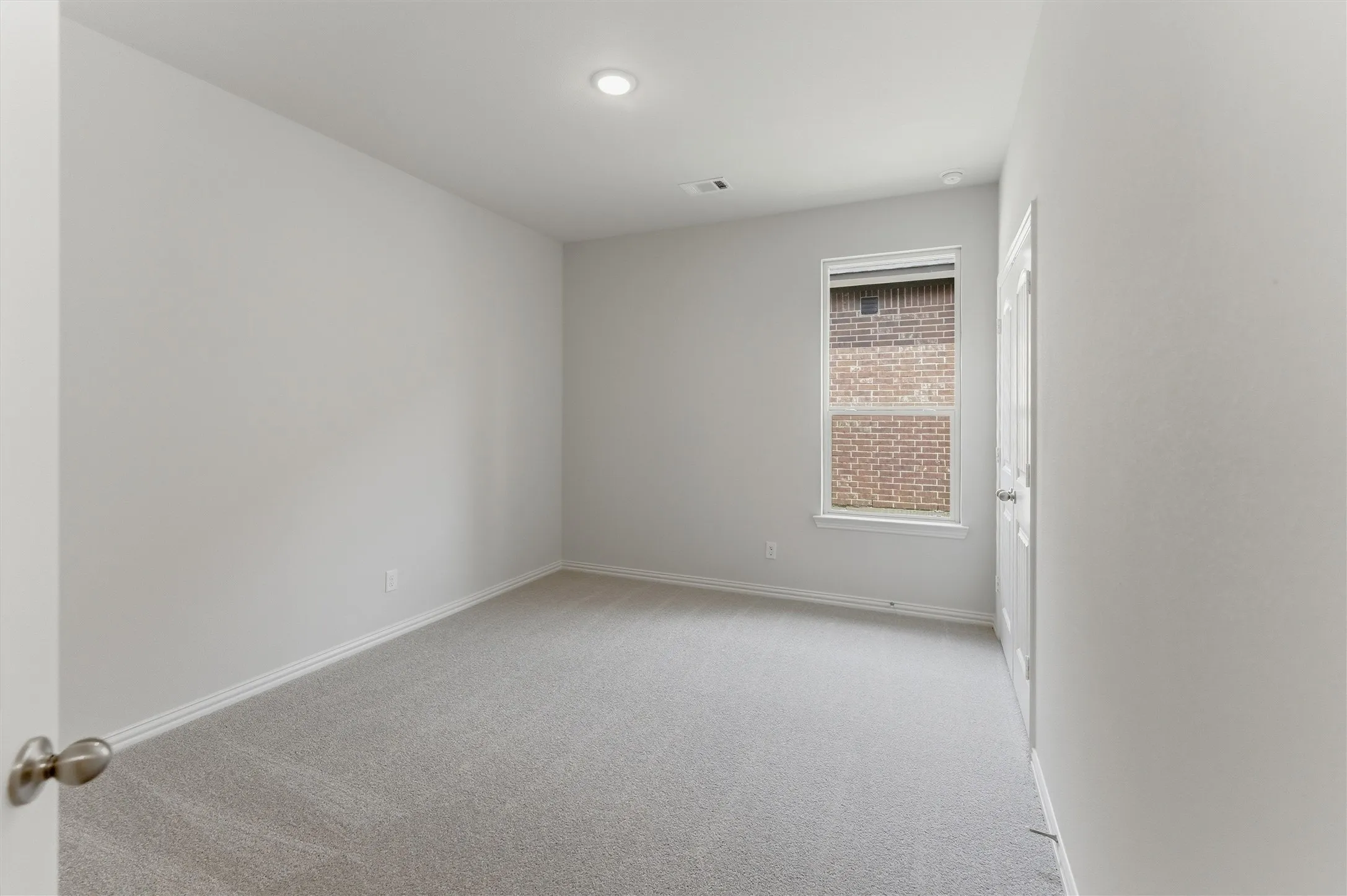 Spacious room featuring light gray carpeting, neutral wall paint, a single window with white trim, and a ceiling-mounted recessed light
