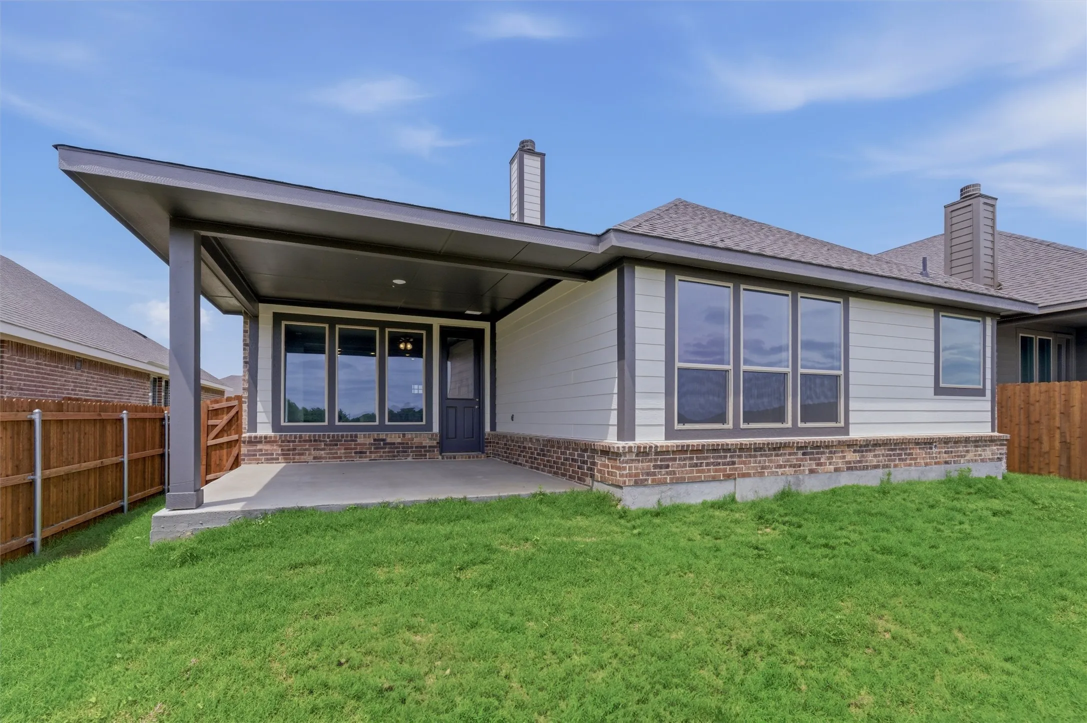 Covered patio with concrete flooring, brick foundation, wood siding, and multiple windows