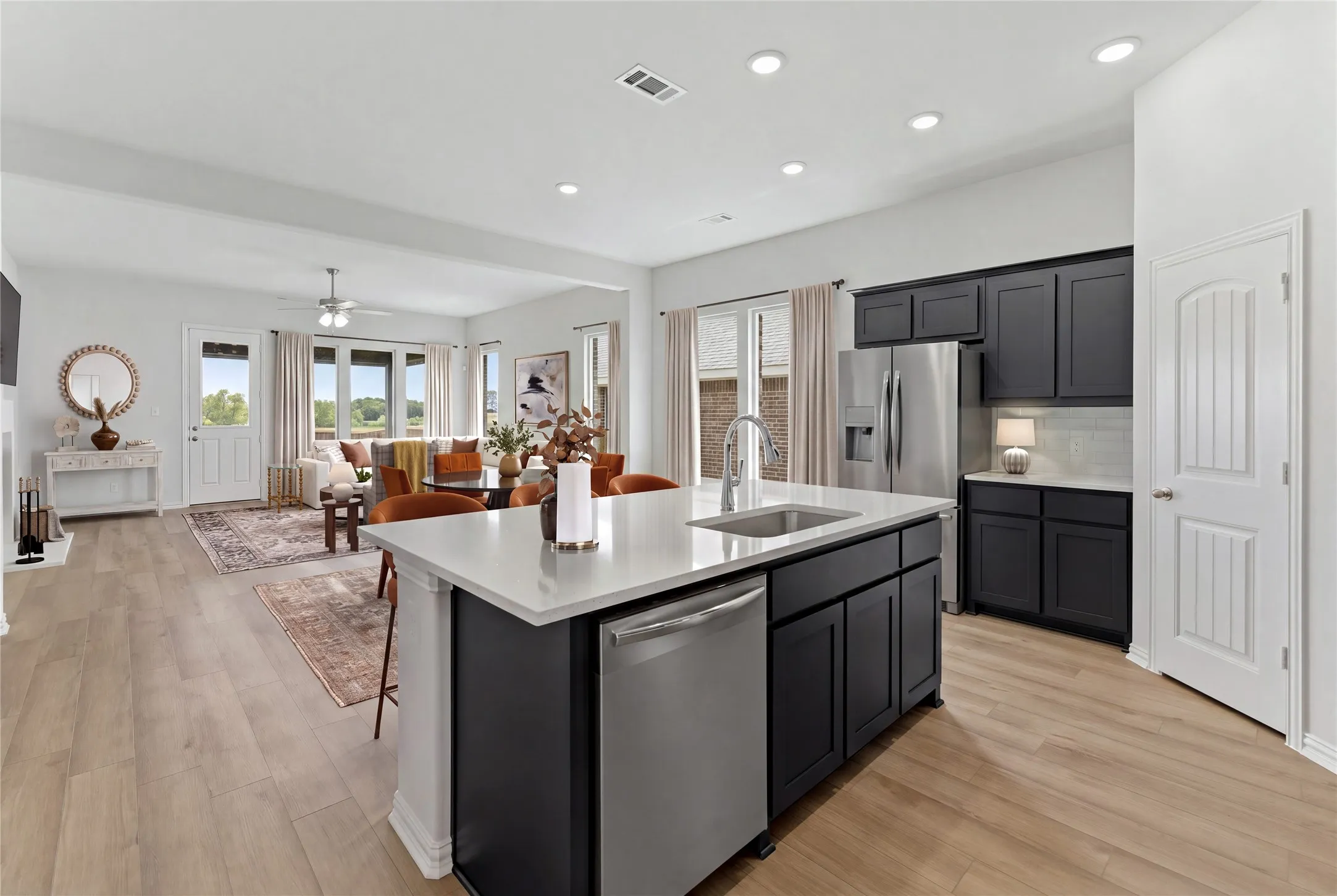 Open-concept living space with wood-finish flooring, a kitchen island featuring a stainless-steel sink and dishwasher, dark cabinetry, and recessed lighting