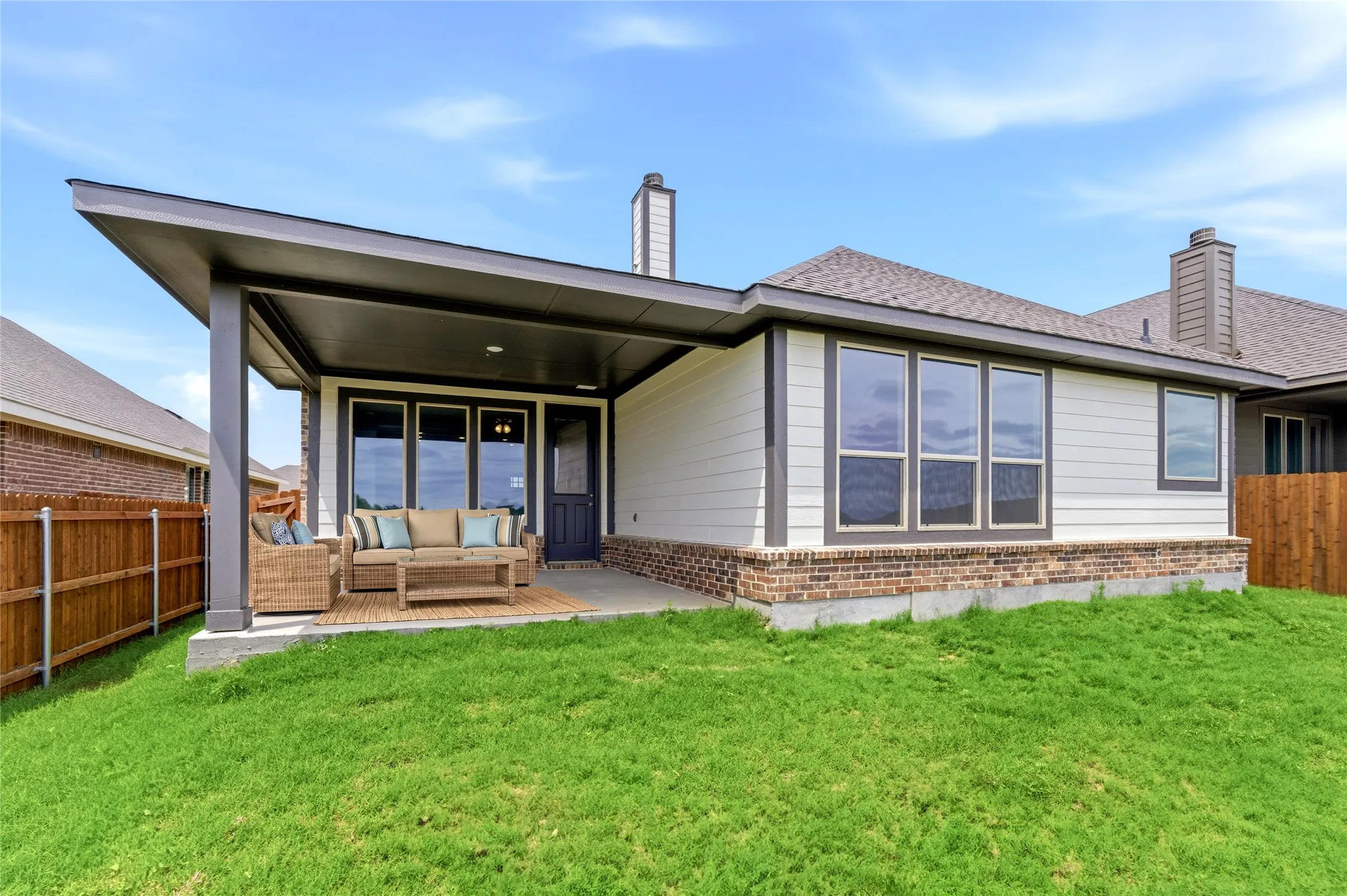 Covered patio with a dark grey flat roof, white siding, and a brick foundation