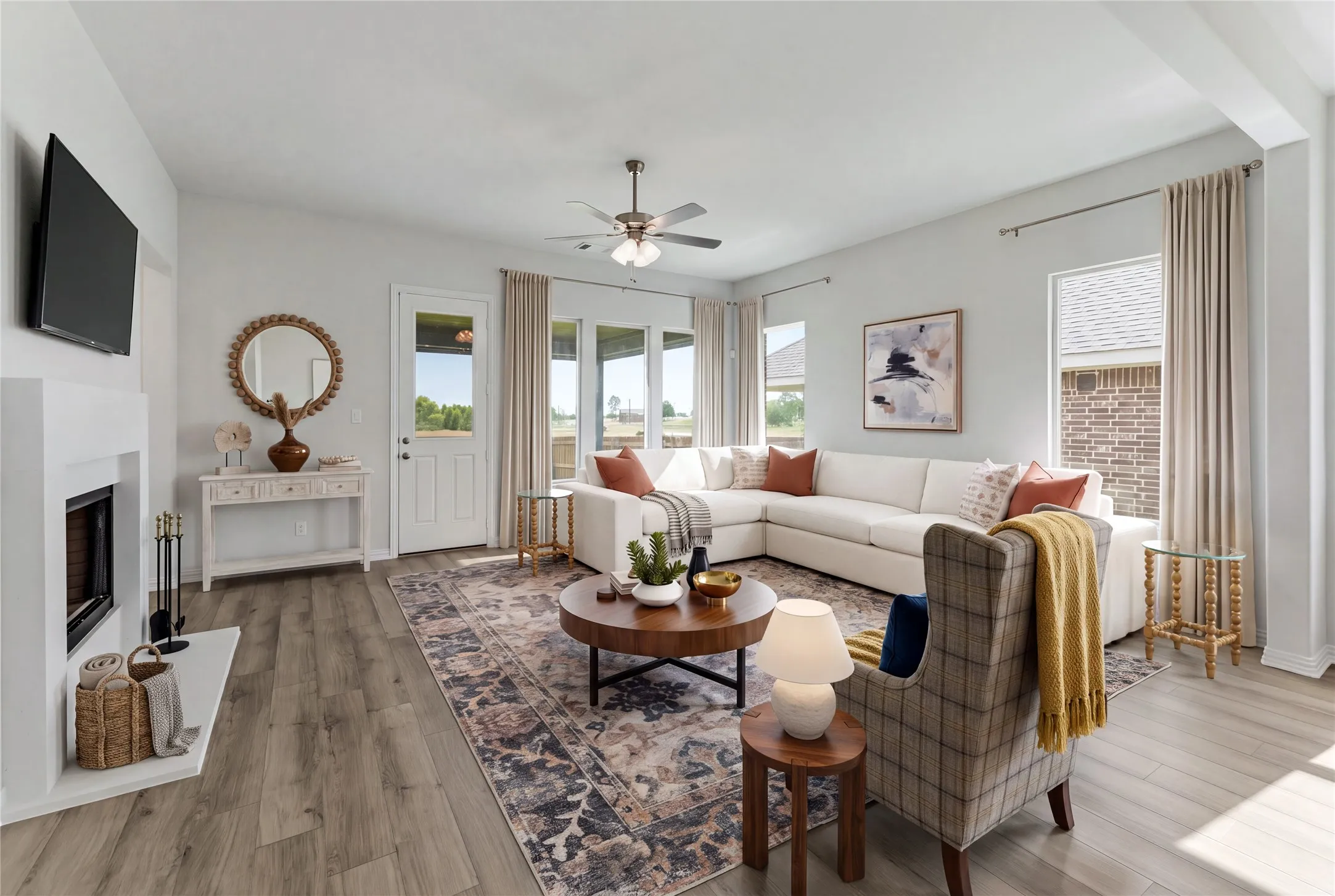 Spacious living area featuring wood-finish flooring, a white fireplace with hearth, multiple windows, and a ceiling fan