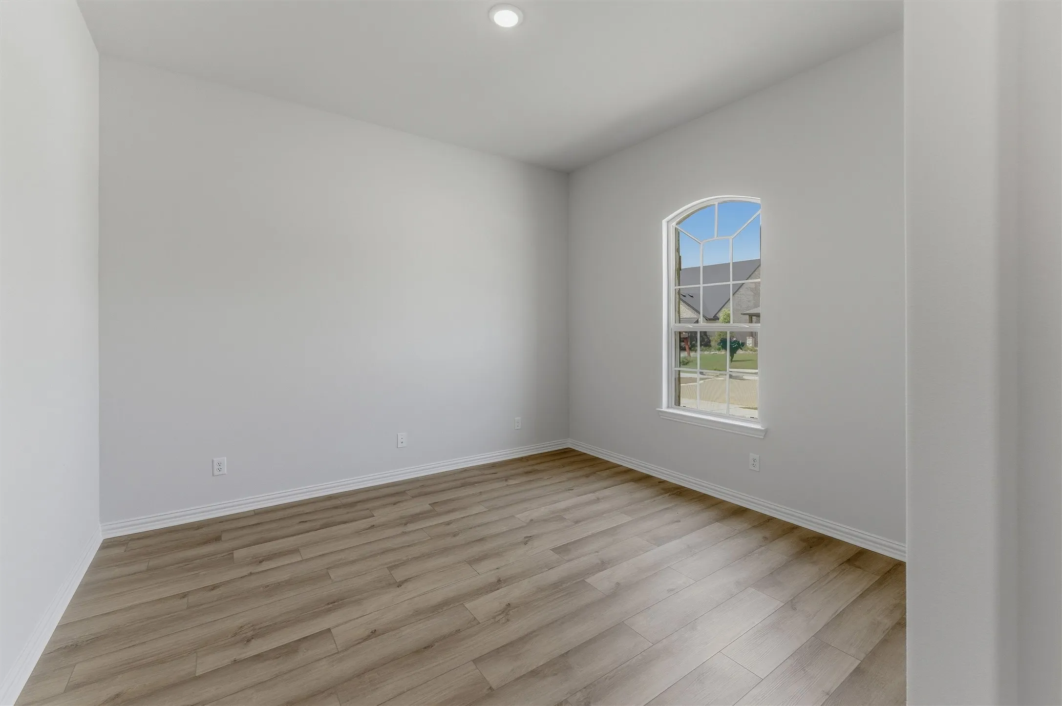 Room featuring wood-finish flooring, white baseboards, and a single arched window with grid panes