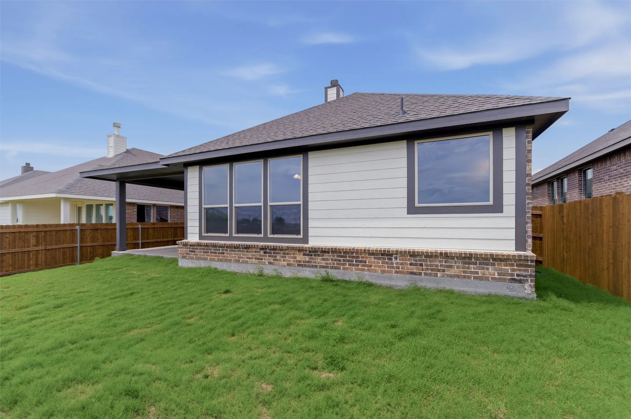 Expansive green lawn with a newly constructed exterior featuring white siding, a dark shingle roof, and a brick base