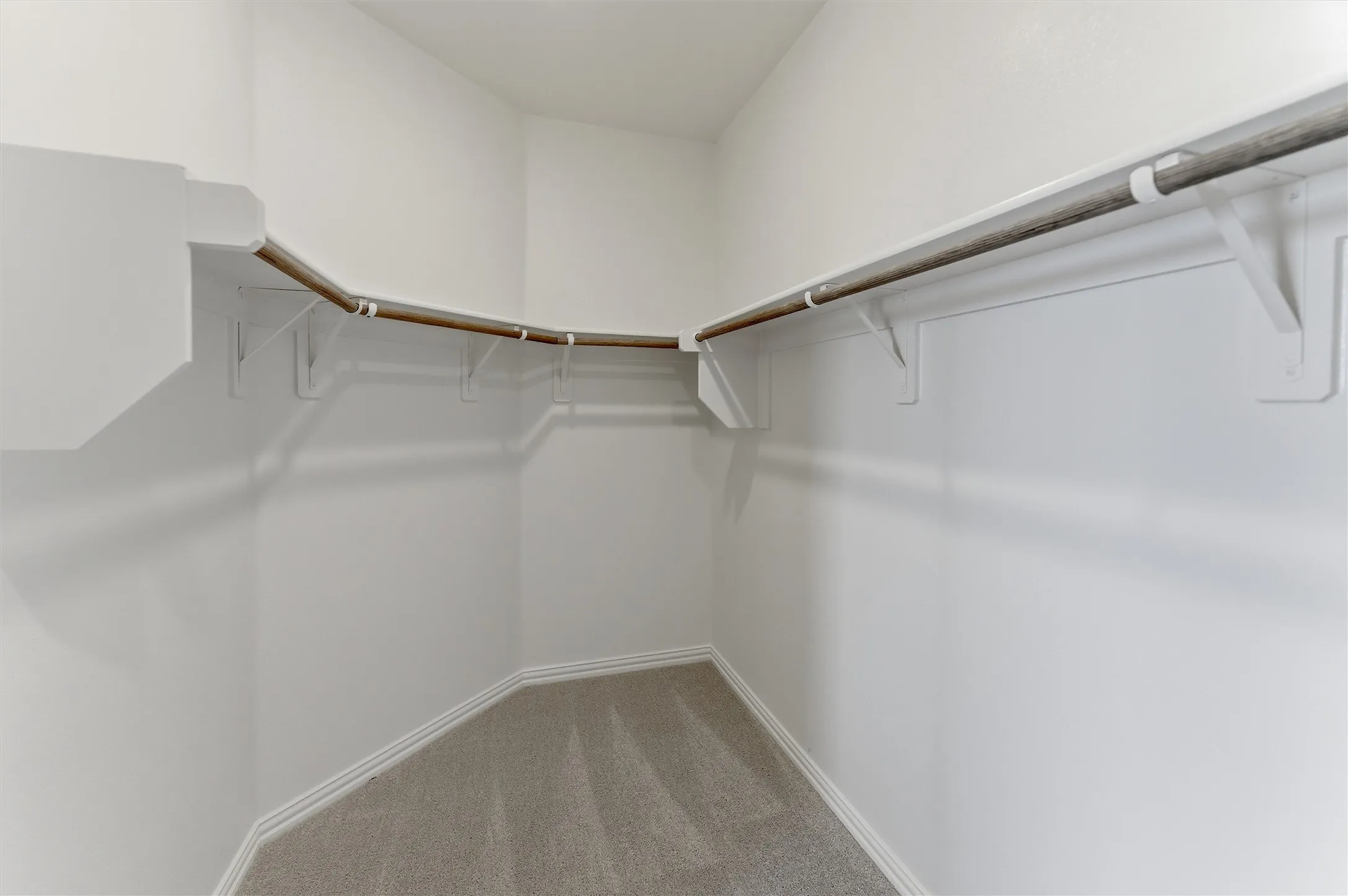 Walk-in closet featuring light gray carpeting, white baseboards, and white shelving with hanging rods
