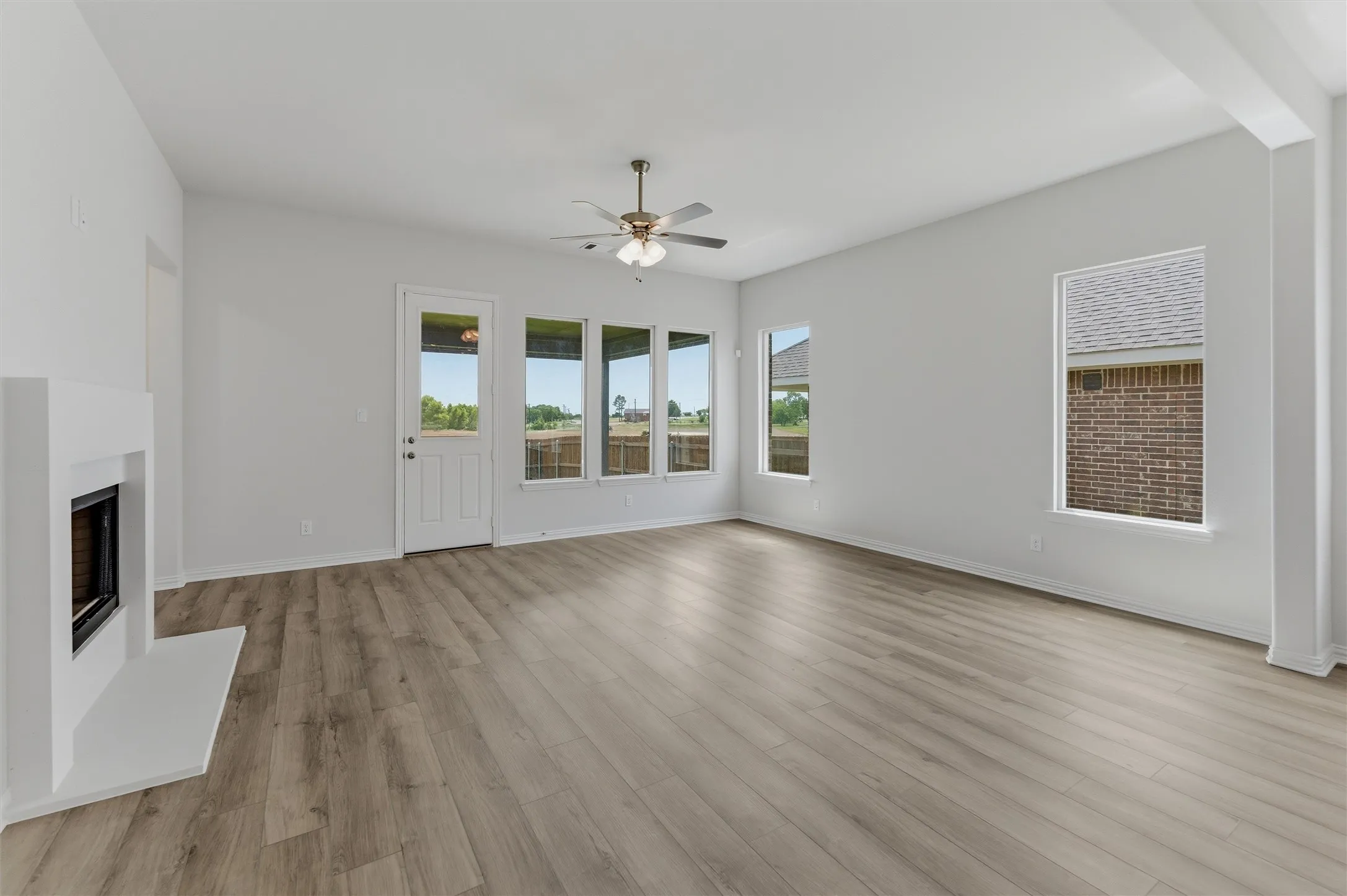 Spacious living area featuring light wood-finish flooring, a contemporary fireplace with a white surround, and multiple windows providing ample natural light