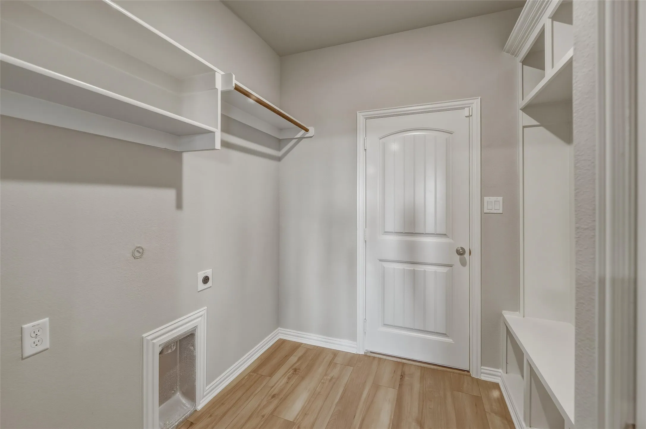 Laundry area featuring wood-finish flooring, built-in shelving, and a hanging rod