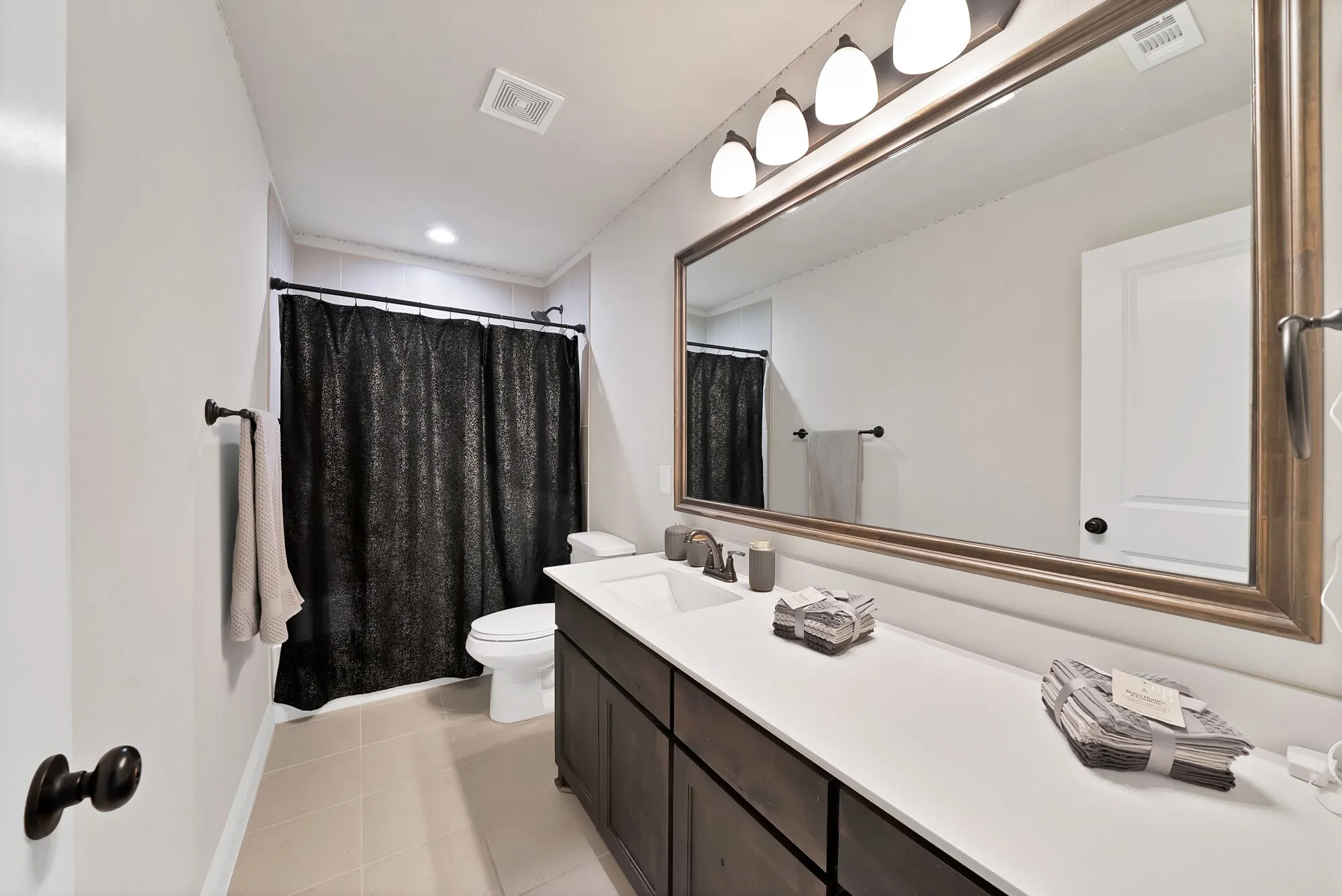 Bathroom featuring a vanity with a white countertop and dark wood cabinetry, a large mirror with a decorative frame, and overhead lighting