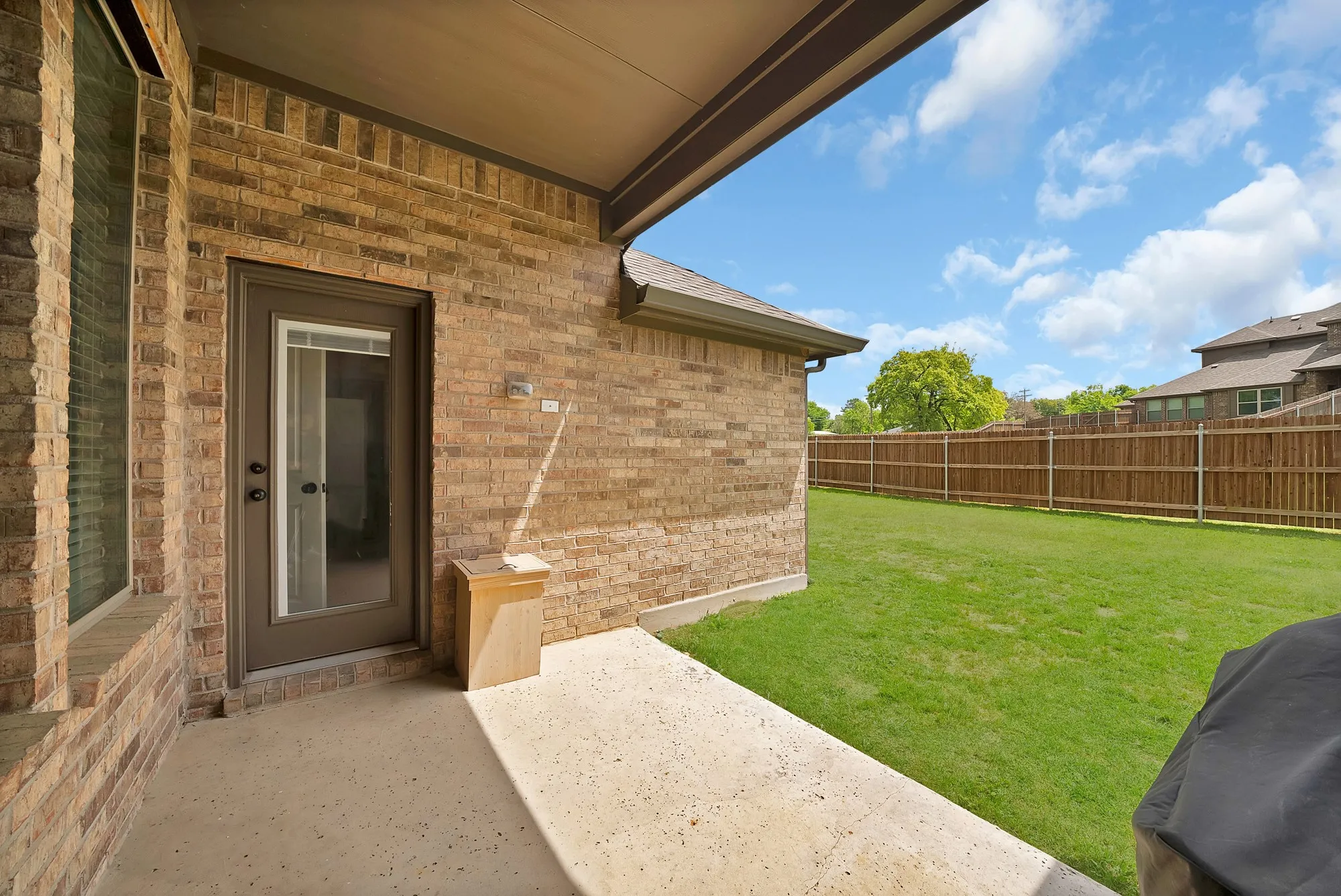 The property features a covered patio with a concrete surface, a brick exterior, and a glass-paneled door