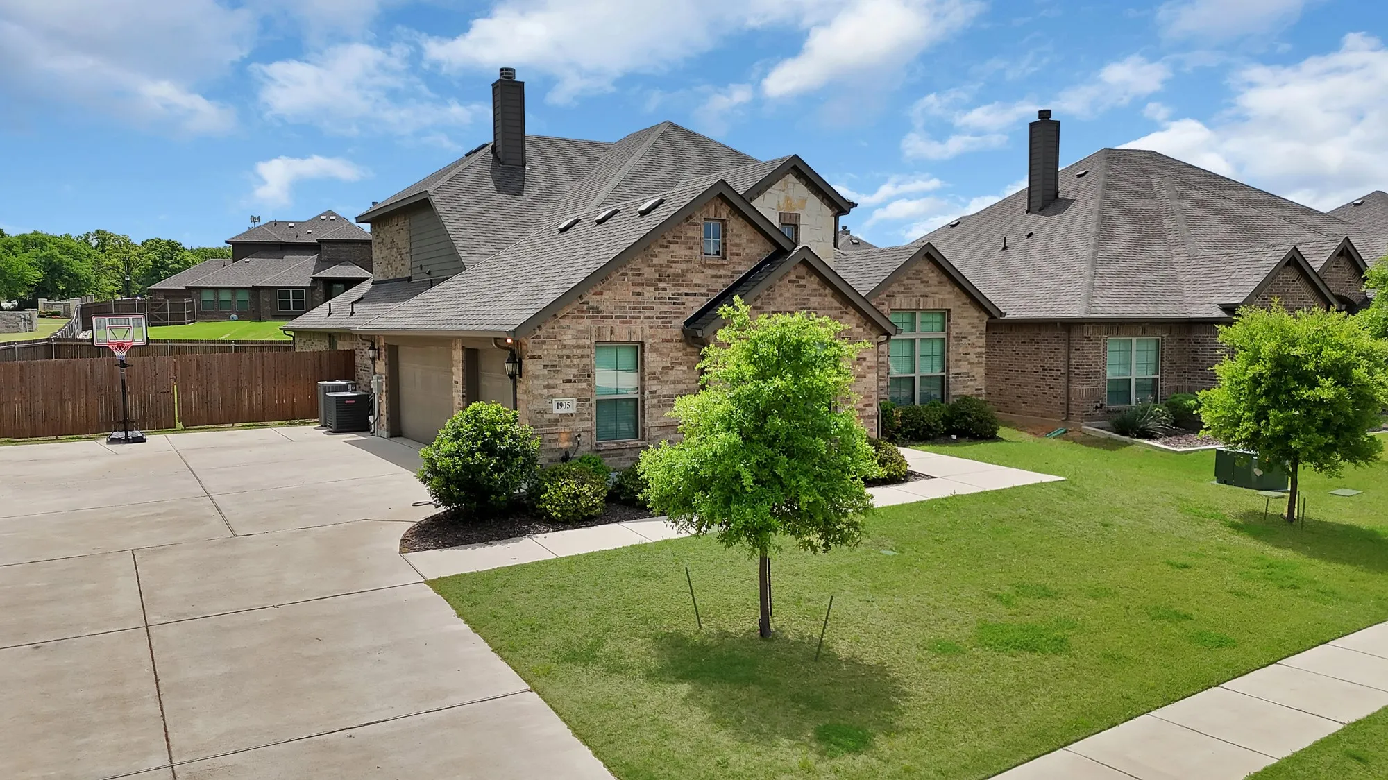 The property features a brick exterior, a driveway, and a front yard with a lawn and trees