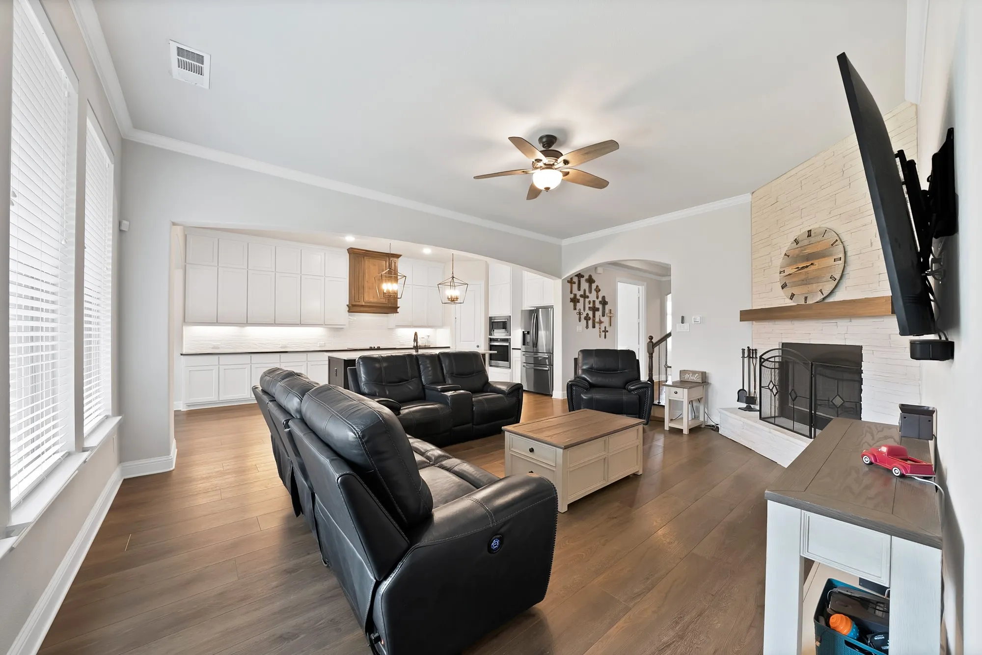 The spacious living area features hardwood flooring, a white brick fireplace with a wood mantle, and a ceiling fan
