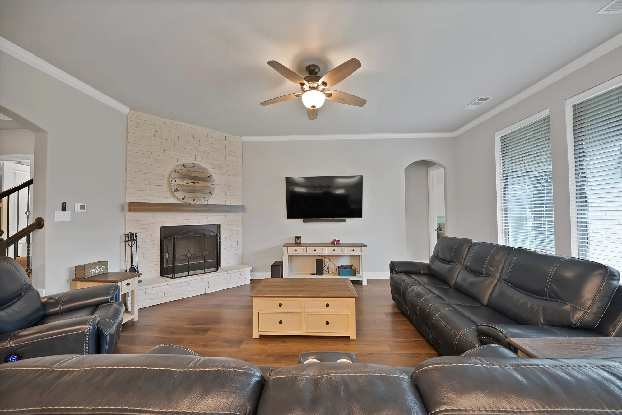 Living area featuring hardwood flooring, a corner fireplace with a white brick surround and wood mantel, crown molding, and a ceiling fan
