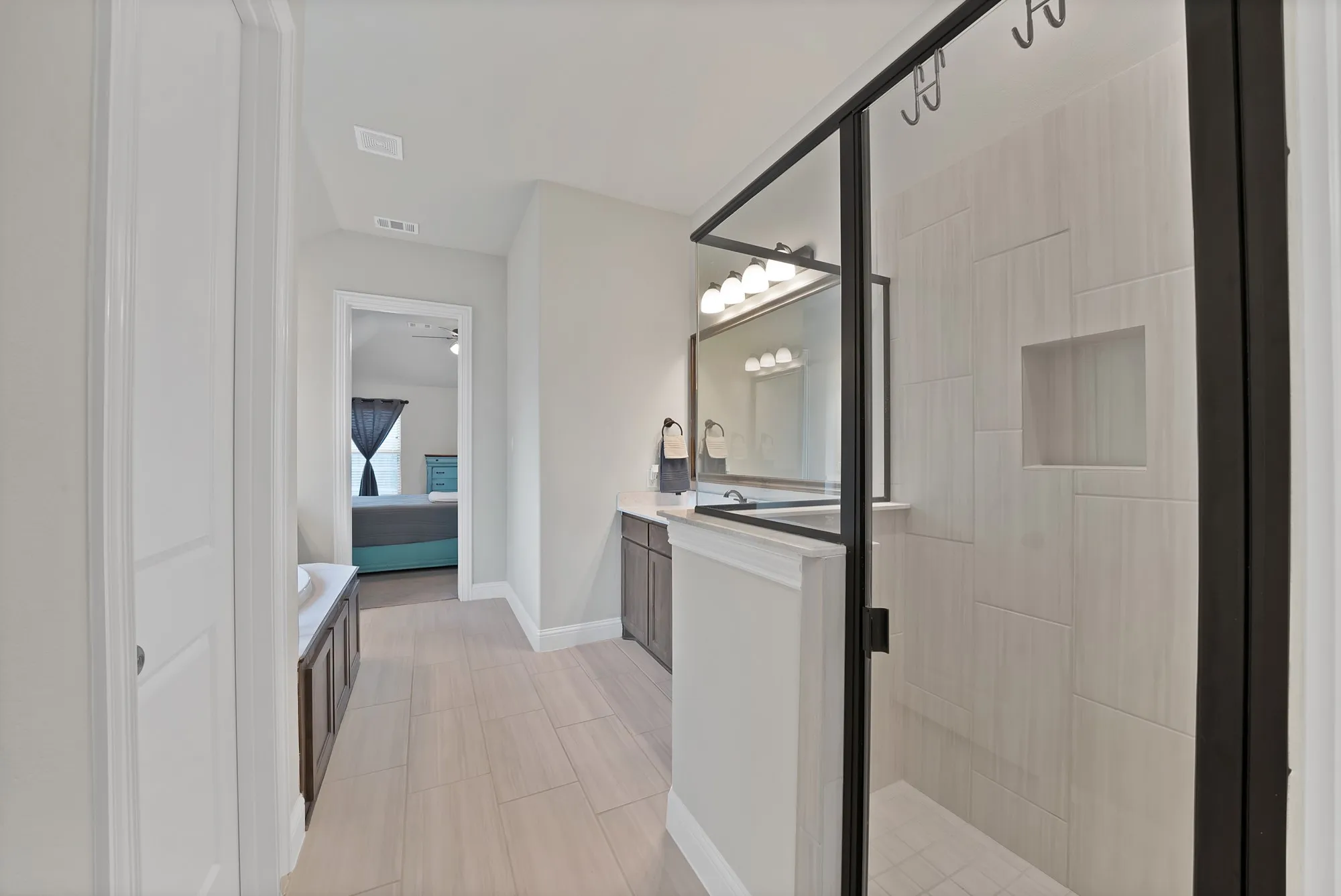 The bathroom features a spacious shower with a clear glass enclosure and light-colored tile work, a vanity with a mirror and lighting, and light wood-look flooring