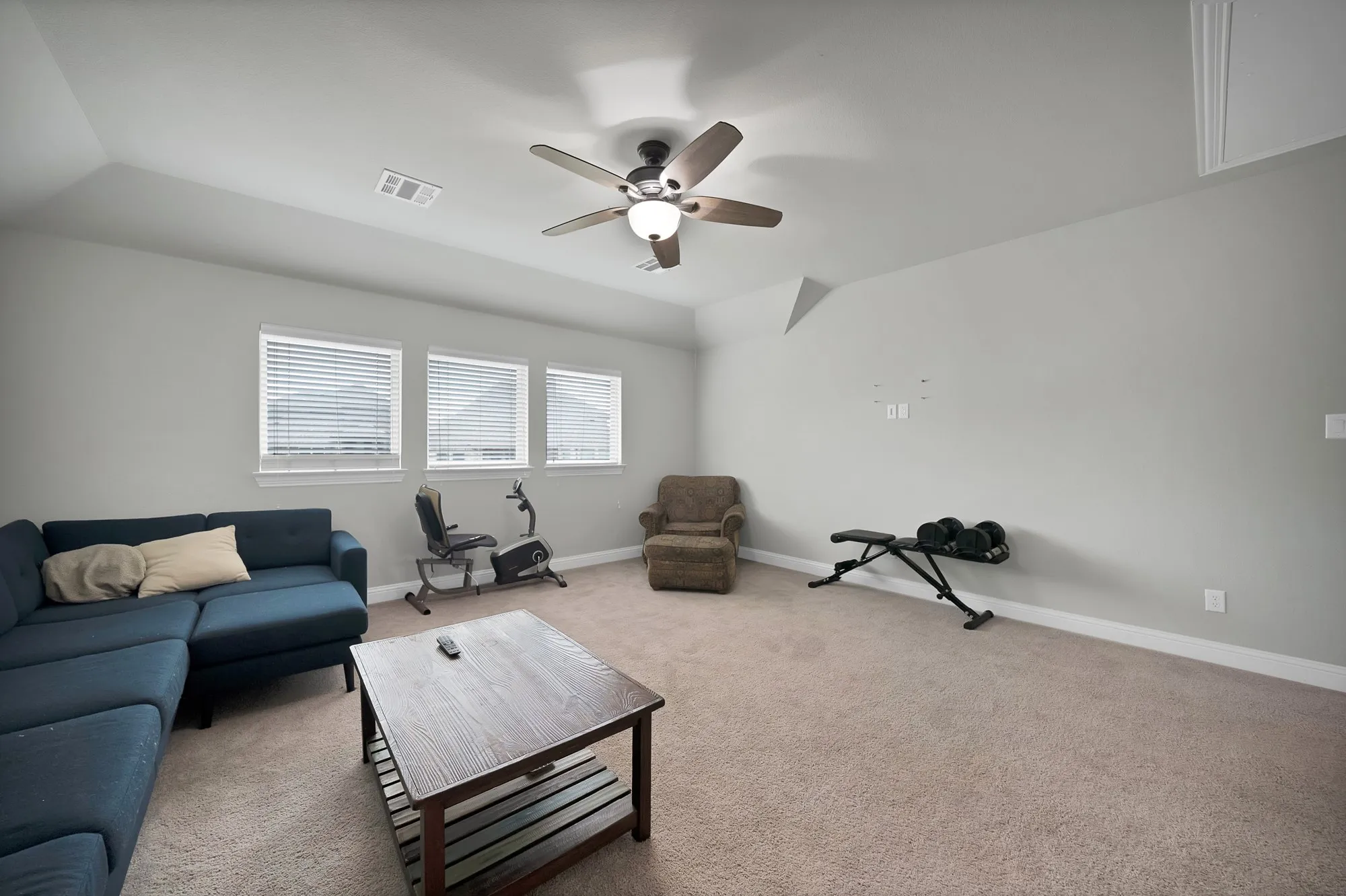 Well-lit room featuring three windows with blinds, a ceiling fan with light, and carpeted flooring