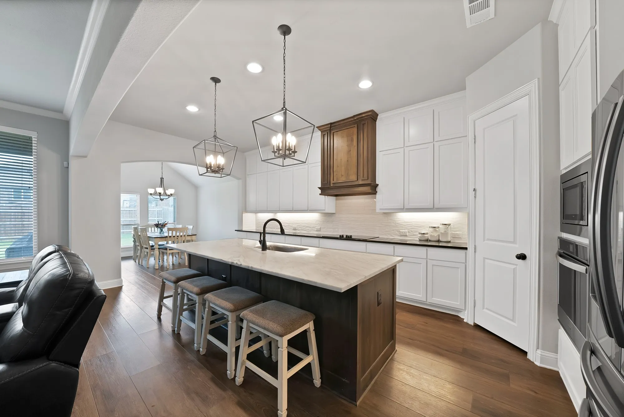 The kitchen features a large island with seating, white cabinetry, dark countertops, and stainless steel appliances