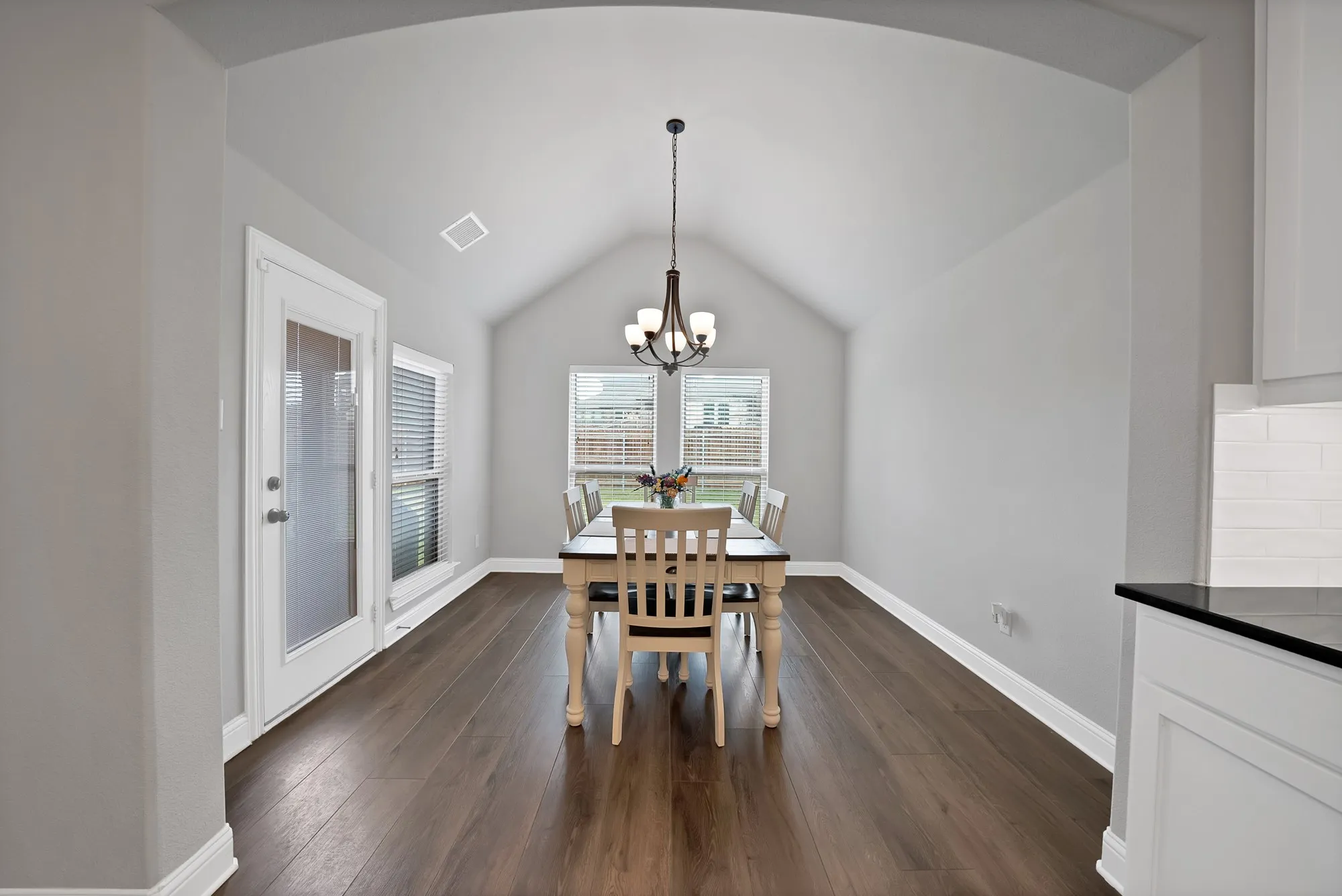Dining area featuring vaulted ceilings, a contemporary chandelier, and rich wood flooring