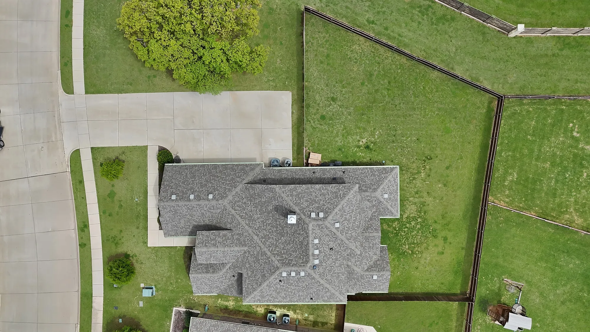 The property features a large roof with multiple gables, a spacious concrete driveway, and extensive green lawn areas