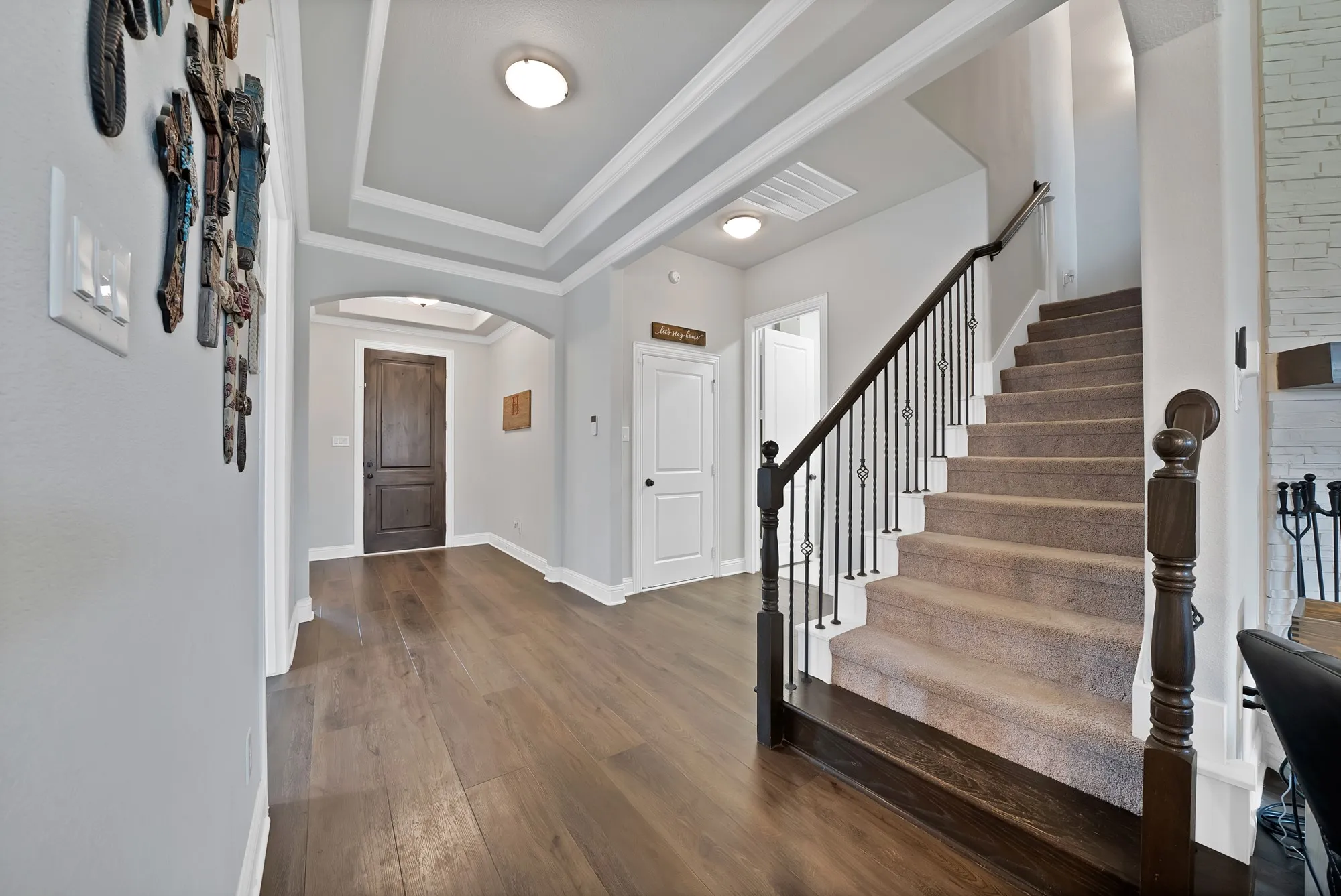 Entryway featuring hardwood floors, a tray ceiling, an arched doorway, and a carpeted staircase with a dark wood and wrought iron railing