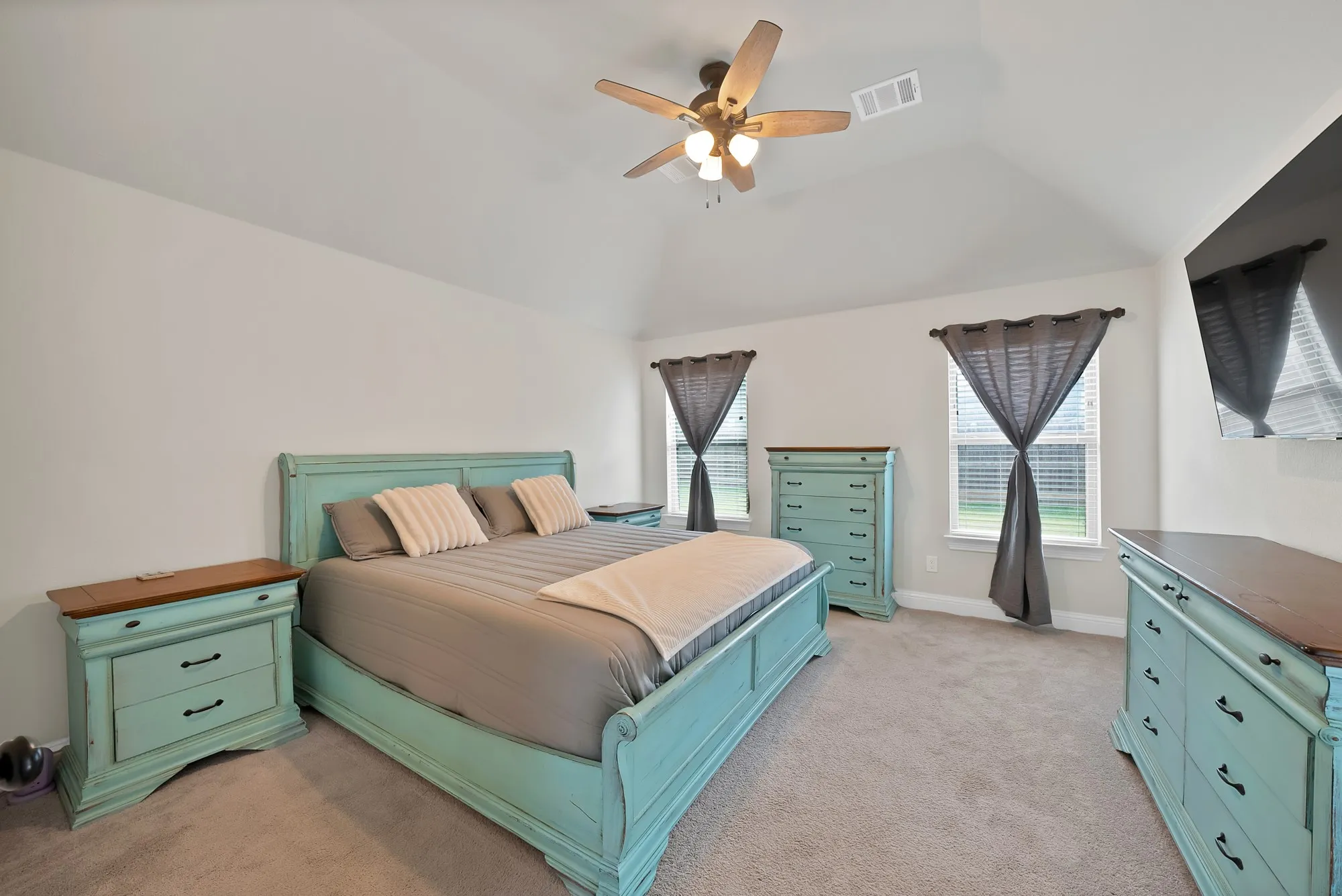 This bedroom features a vaulted ceiling with a ceiling fan, two windows with blinds, and carpeted flooring