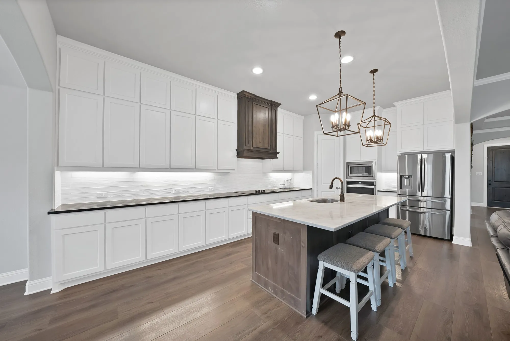 The kitchen features an expansive island with a light-colored countertop, white cabinetry, stainless steel appliances, and two decorative pendant lights