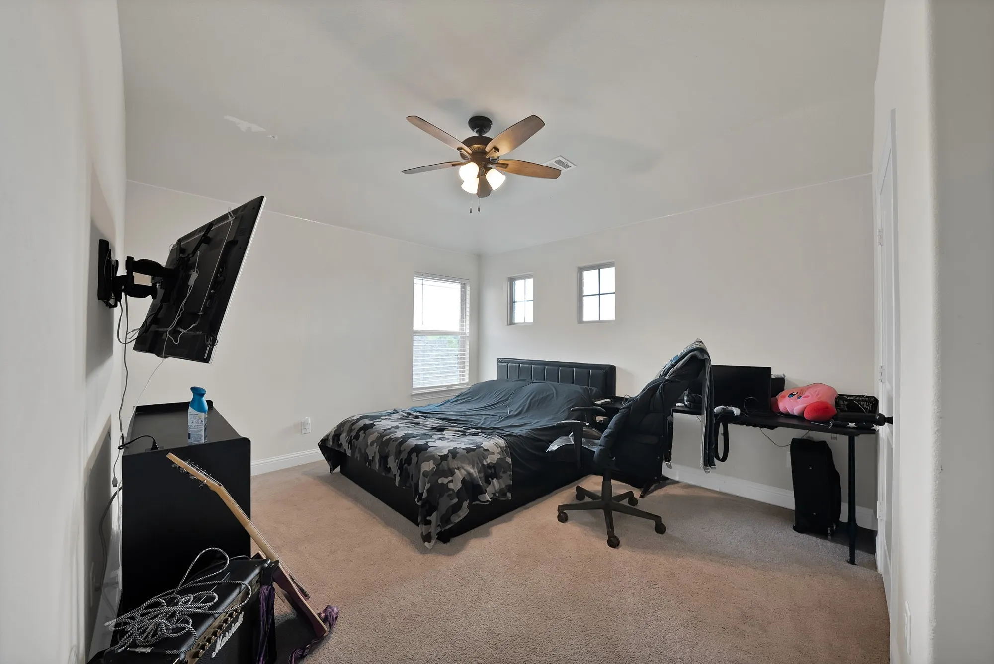 This room features light neutral-toned walls and carpeting, a ceiling fan with integrated lighting, and multiple windows allowing for natural light