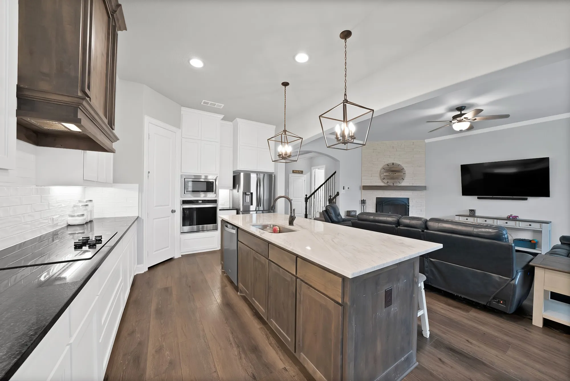 The kitchen features a large island with a light-colored countertop and pendant lighting, stainless steel appliances, and wood flooring