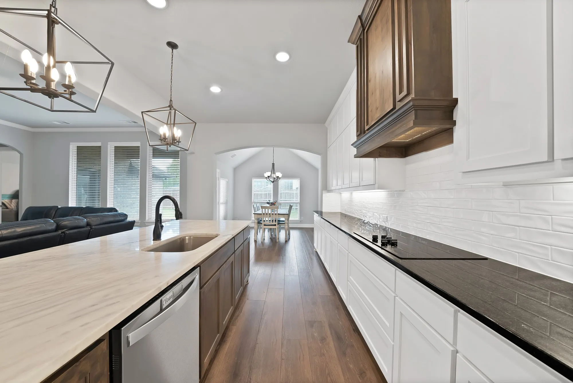 The kitchen features white cabinetry, a dark countertop, and a white subway tile backsplash, with a built-in cooktop and a range hood