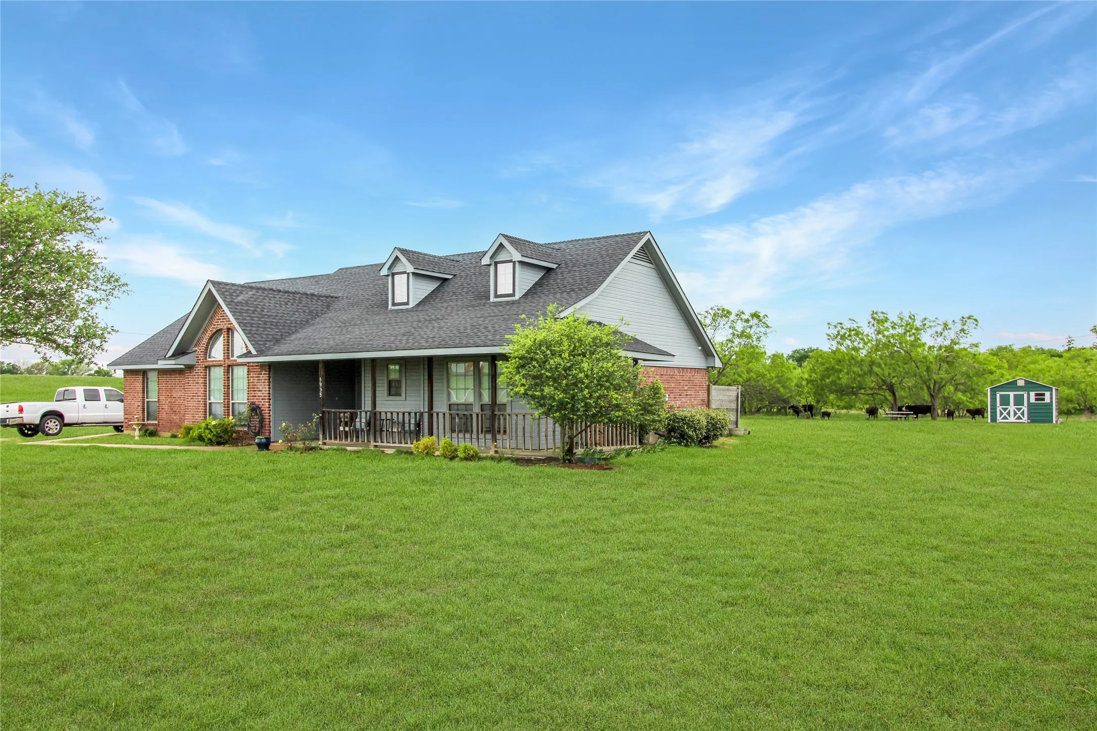 Ranch-style residence featuring a brick and siding exterior, a covered front porch with dark railings, and prominent dormer windows