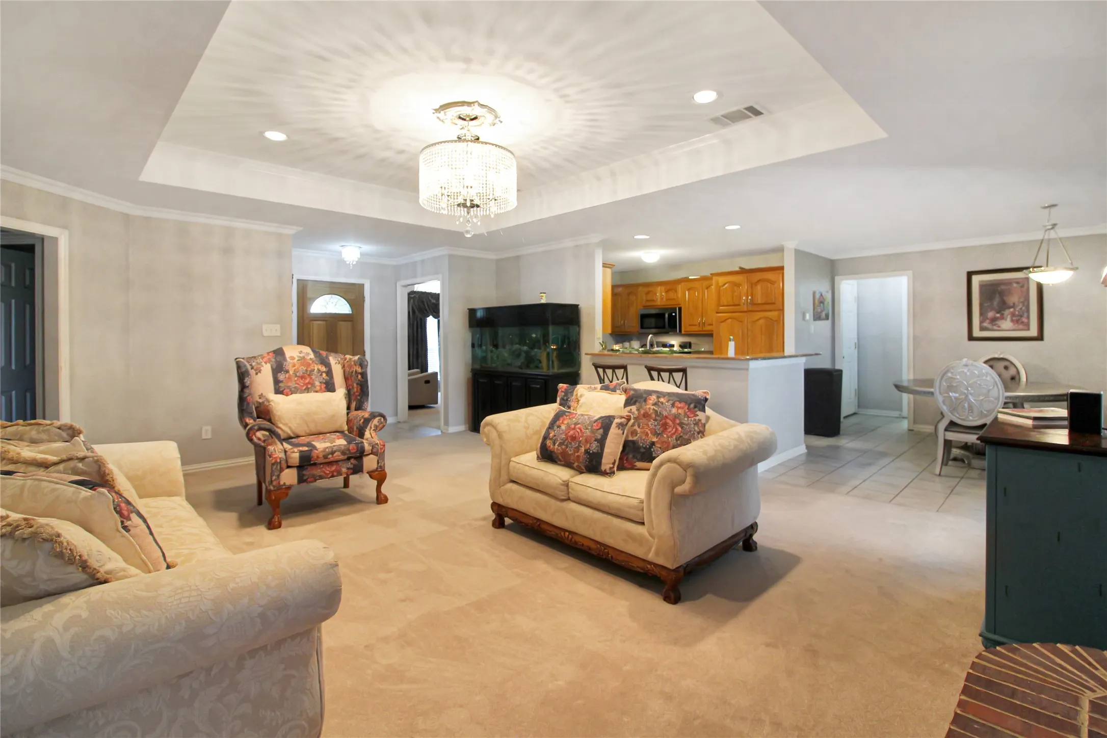 Spacious living area featuring a tray ceiling with an ornate chandelier and recessed lighting