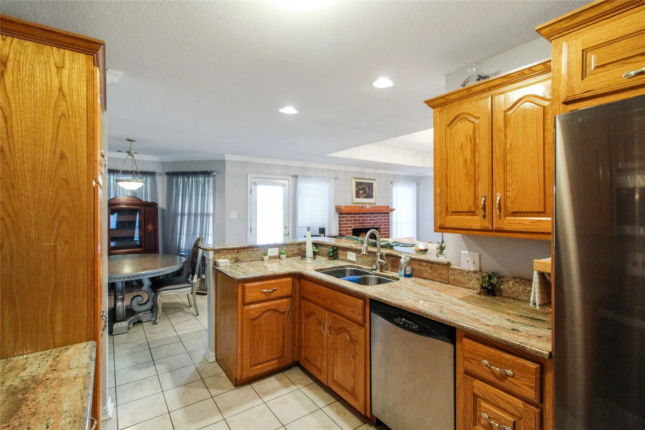 Kitchen featuring wood cabinetry, granite countertops, tile flooring, stainless steel appliances, and a double basin sink with a gooseneck faucet