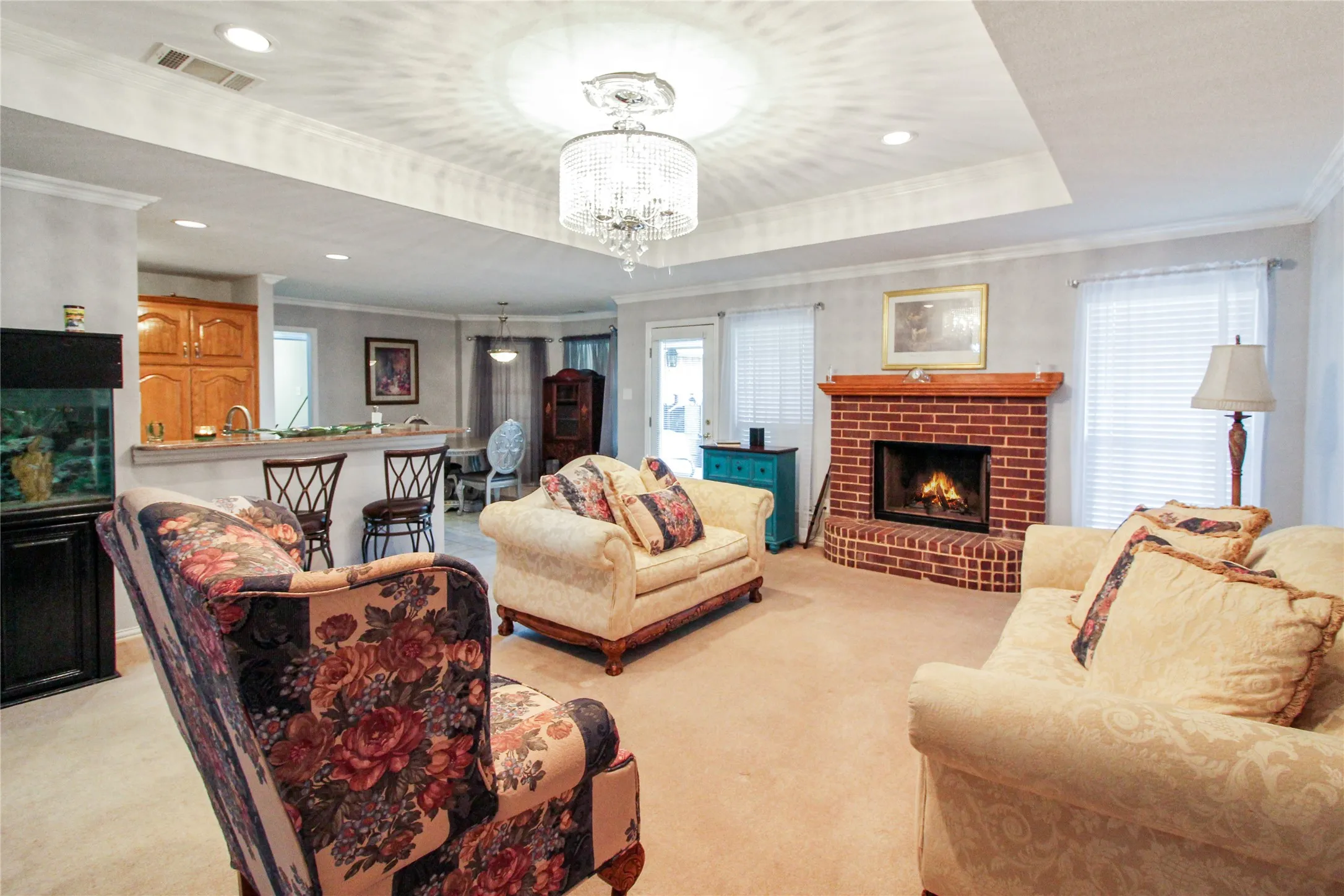 Living area featuring a brick fireplace with a wood mantel, recessed lighting, and a tray ceiling with a chandelier
