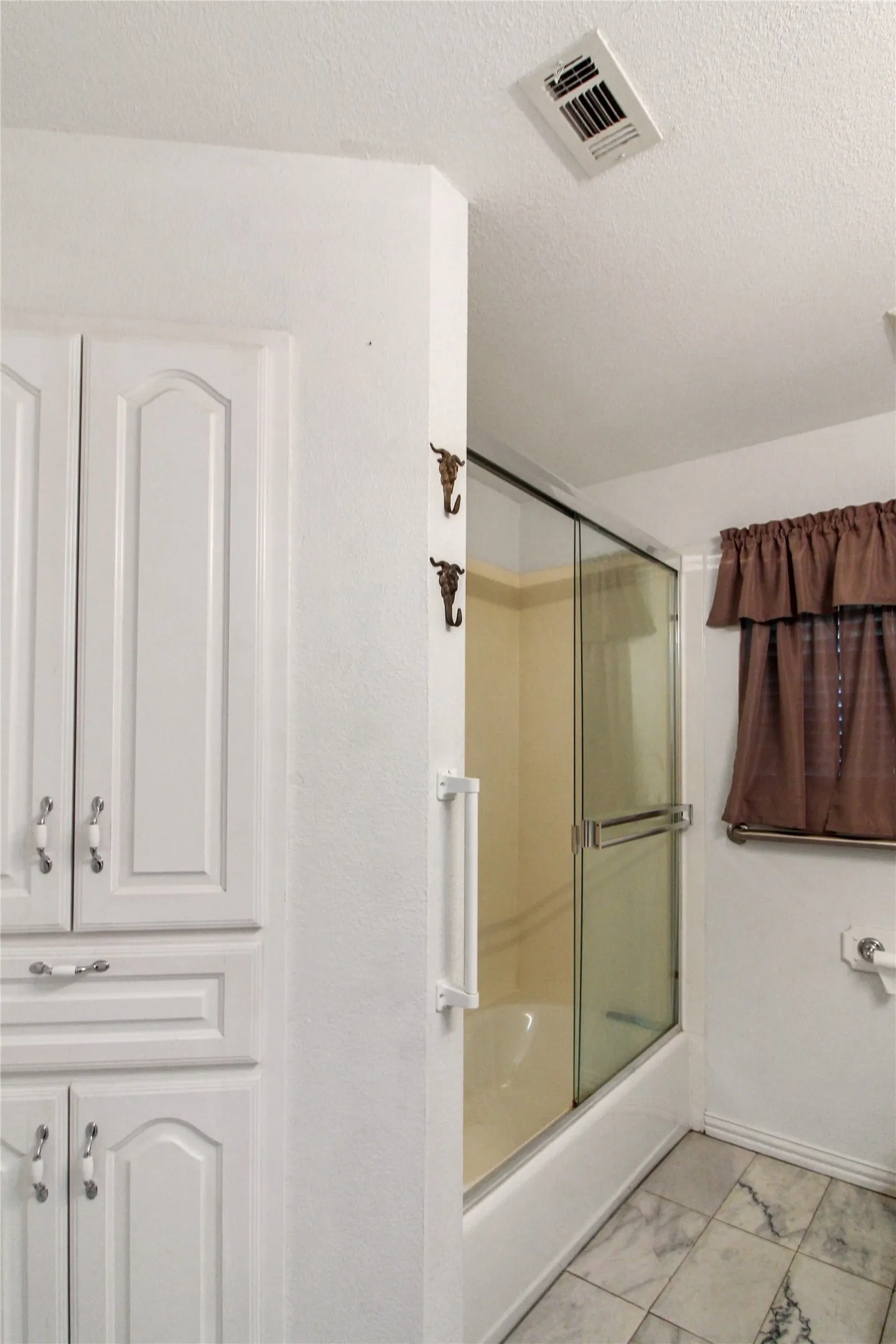 Bathroom featuring a built-in white cabinetry, shower-tub combination with glass enclosure, grab bar, and patterned tile flooring