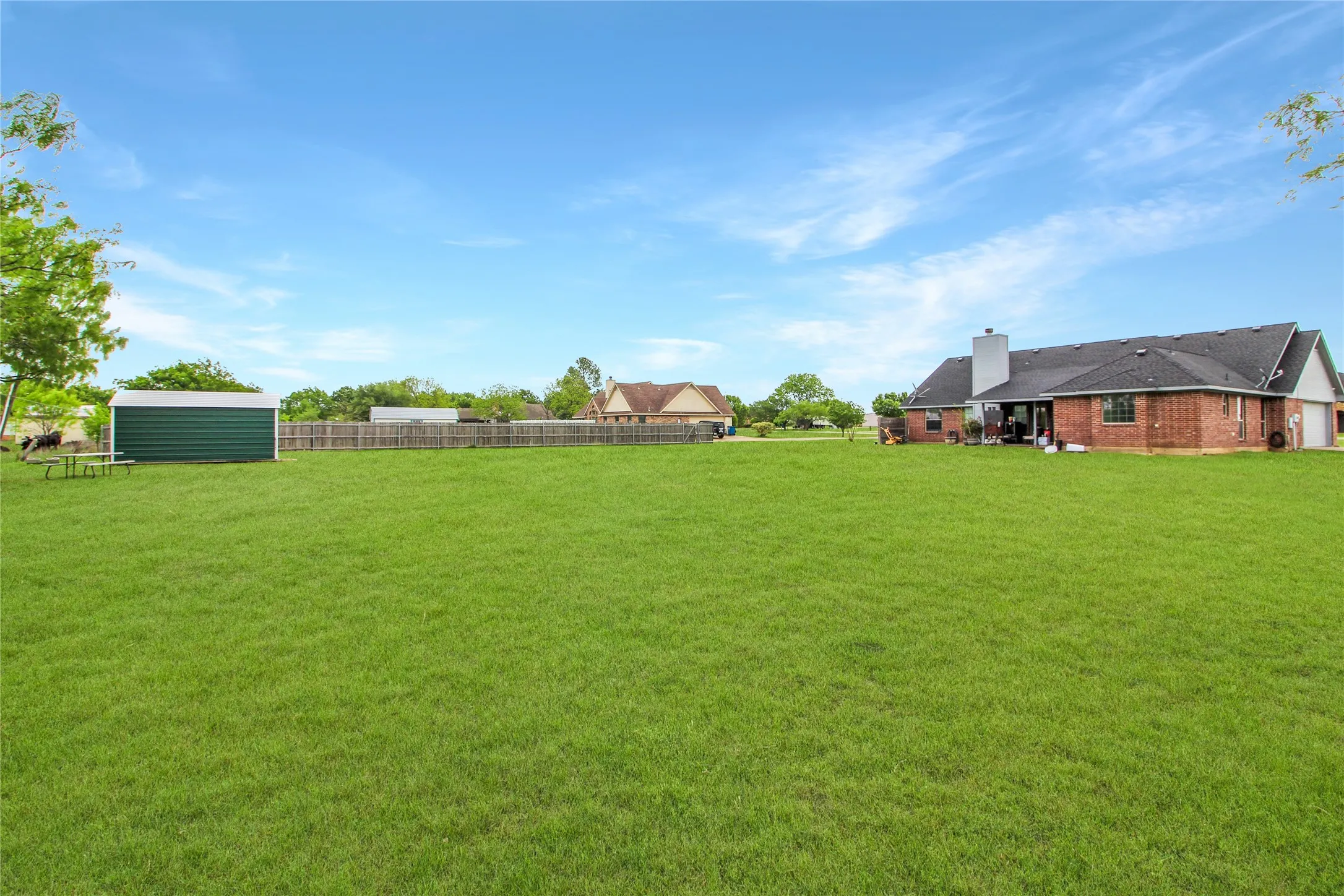 Expansive green lawn with a brick exterior home featuring a dark shingle roof, a white chimney, and an attached garage