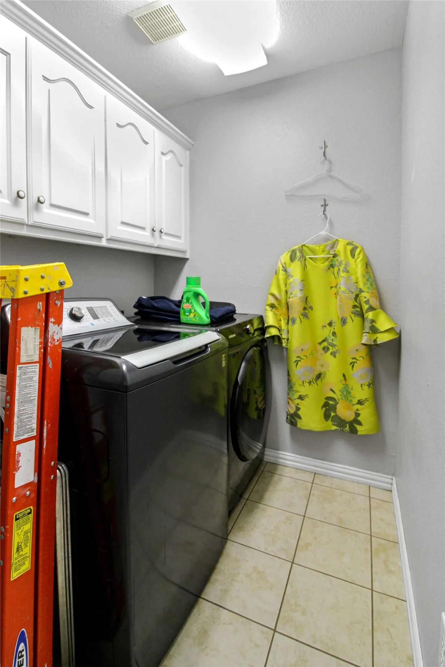 Dedicated laundry space featuring white upper cabinetry, tiled flooring, built-in wall hooks, and ceiling lighting