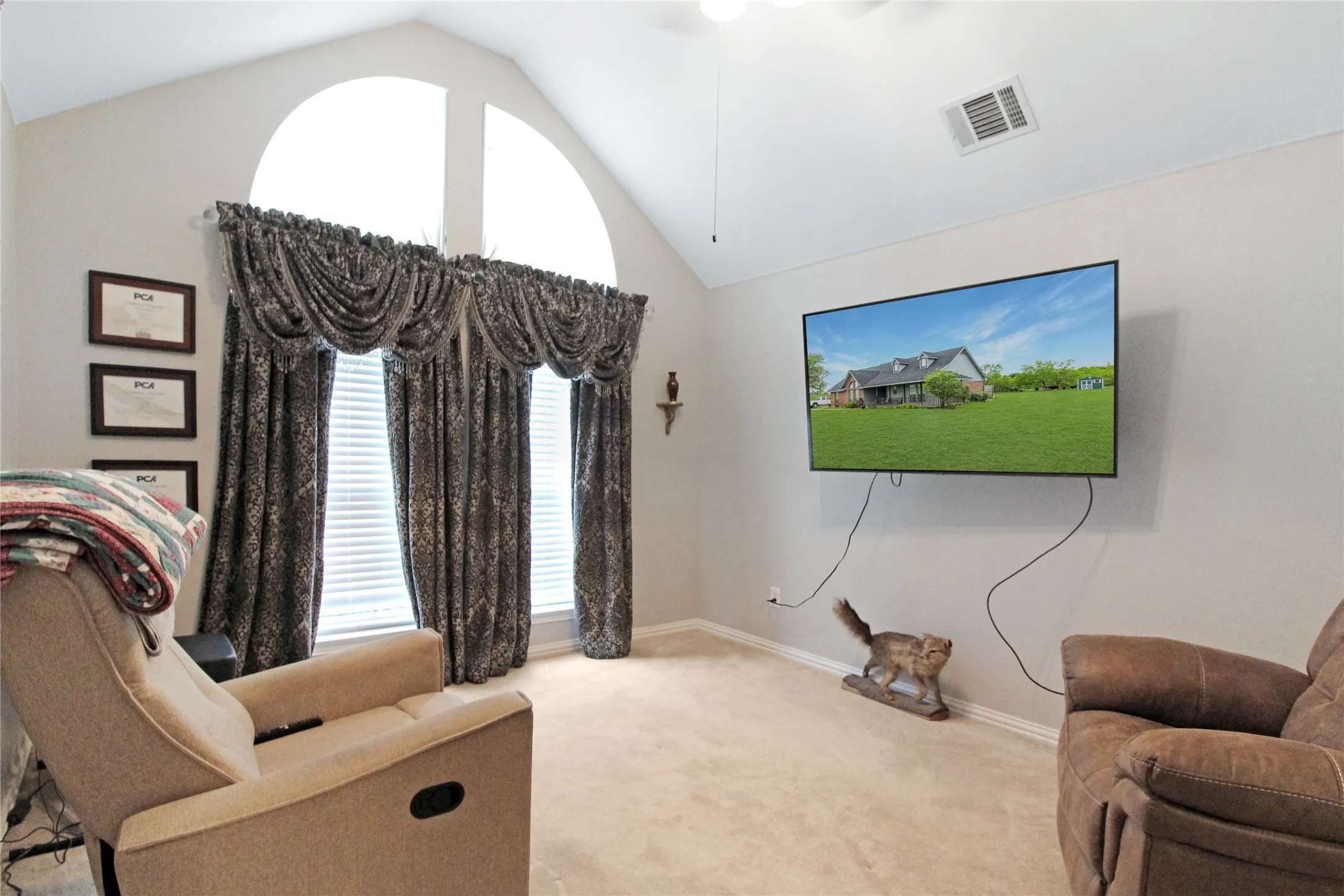 Living area featuring vaulted ceilings, arched transom windows, floor-length window treatments, a ceiling fan, and carpeted flooring