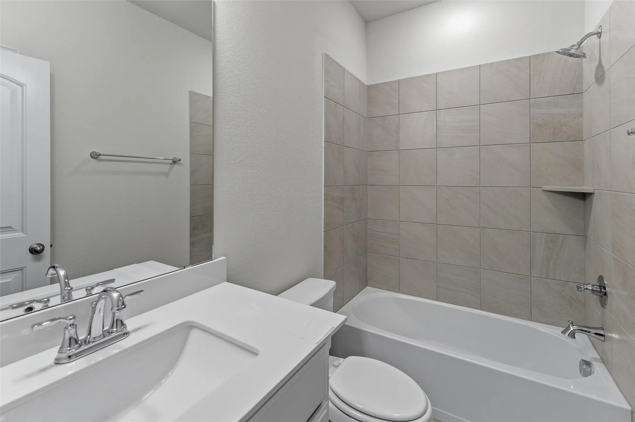 Full bathroom featuring a single vanity with an integrated sink and chrome fixtures, a toilet, and a combination tub and shower with tile surround and a recessed shelf