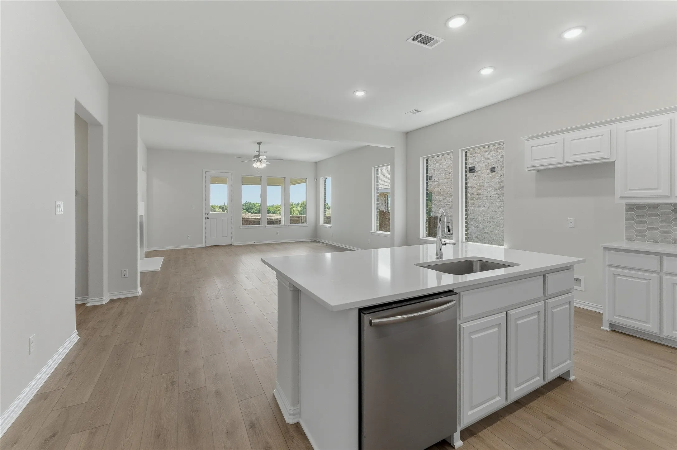 Open-concept living space featuring wood-finish flooring, recessed lighting, and a kitchen island with an integrated stainless steel sink and dishwasher