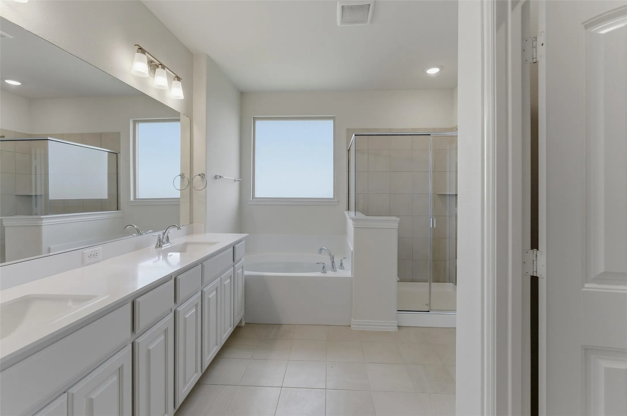 Spacious bathroom featuring a dual vanity with white cabinetry, light-toned countertops, and an oversized mirror