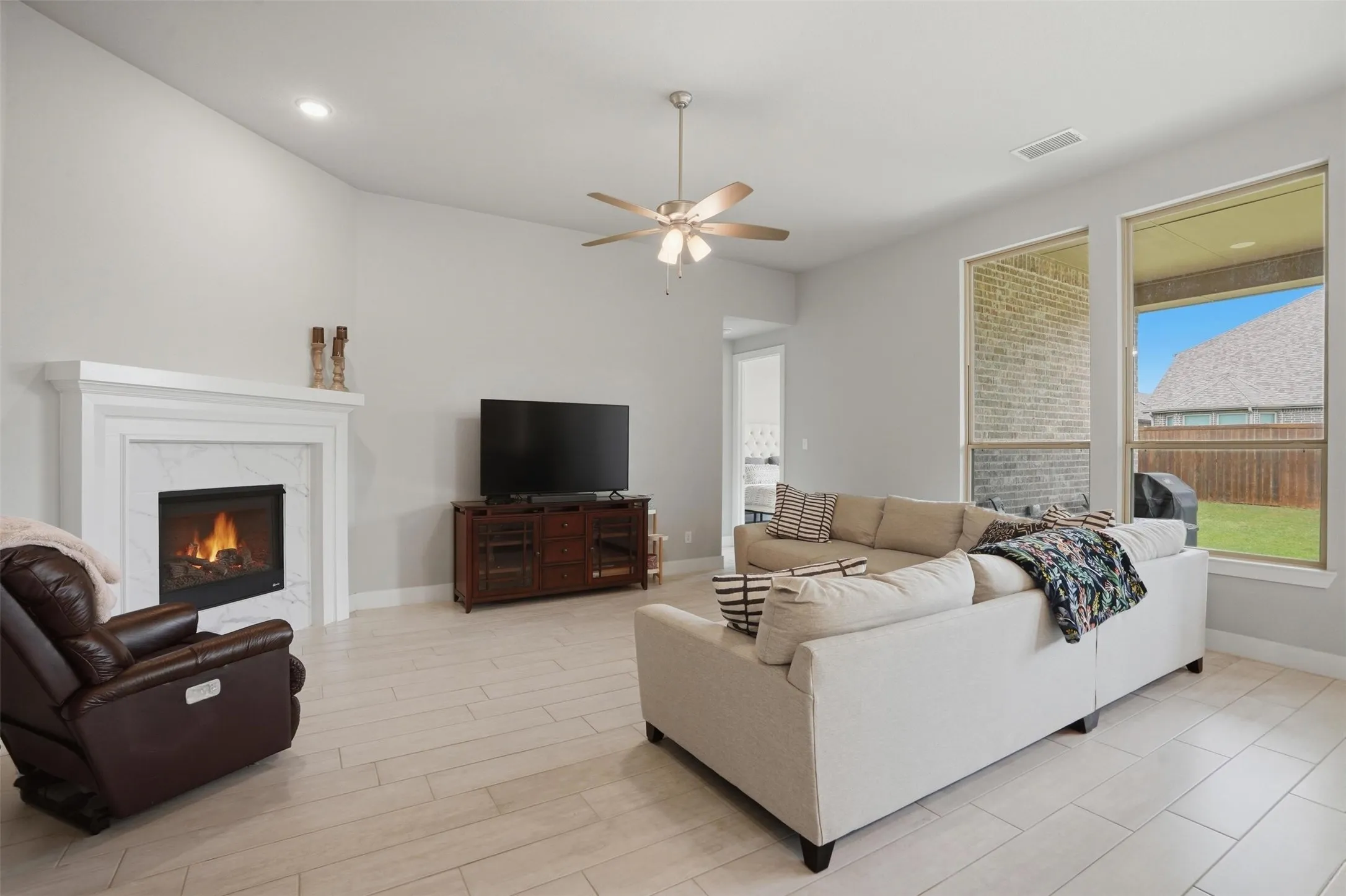 Living area featuring light-colored tile flooring, a fireplace with a white mantel and marble surround, and a ceiling fan