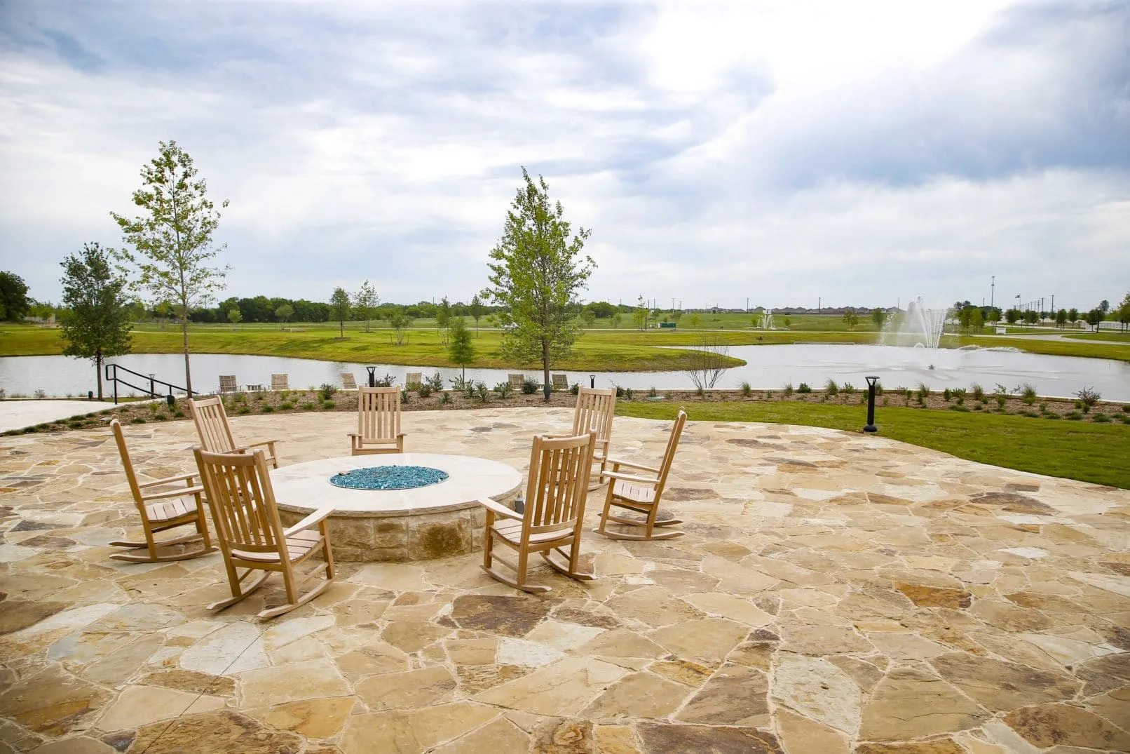 Spacious outdoor patio area featuring flagstone paving, a built-in fire pit with blue fire glass, and several wooden rocking chairs