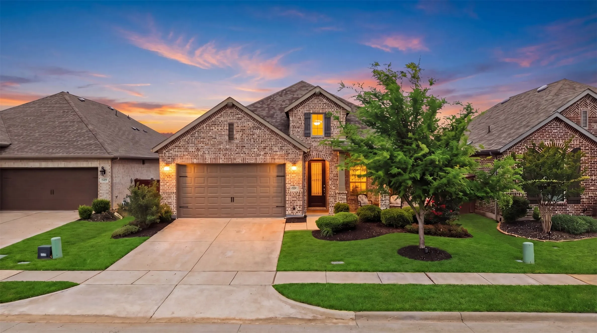The property features a brick facade, a well-maintained front lawn, a paved driveway, and a two-car garage